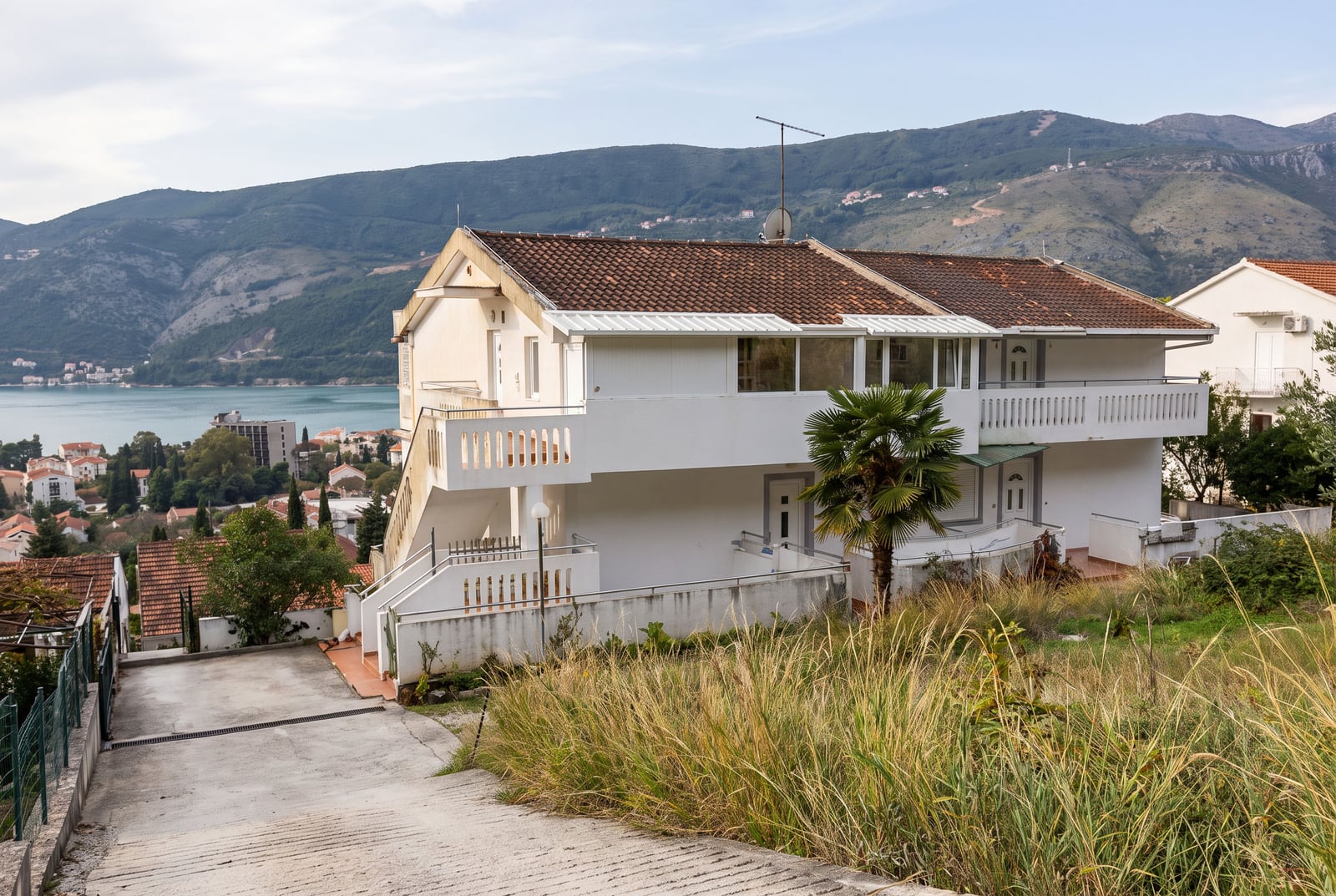 White two-story house with a tiled roof and balconies overlooking the sea and mountains in Igalo, Montenegro