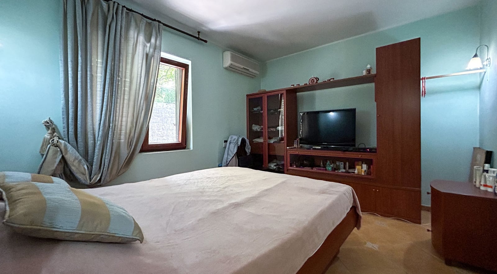 Schlafzimmer mit Doppelbett und Möbeln in einer Villa in Dobrota, Montenegro: Blick auf das Interieur mit TV-Wand und Fenster.
