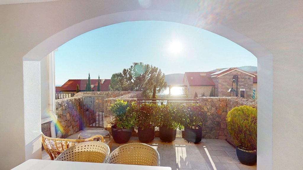 Terrasse mit Steinverkleidung und Meerblick im Wohnkomplex Luštica, Montenegro: Korbmöbel und Pflanzen.