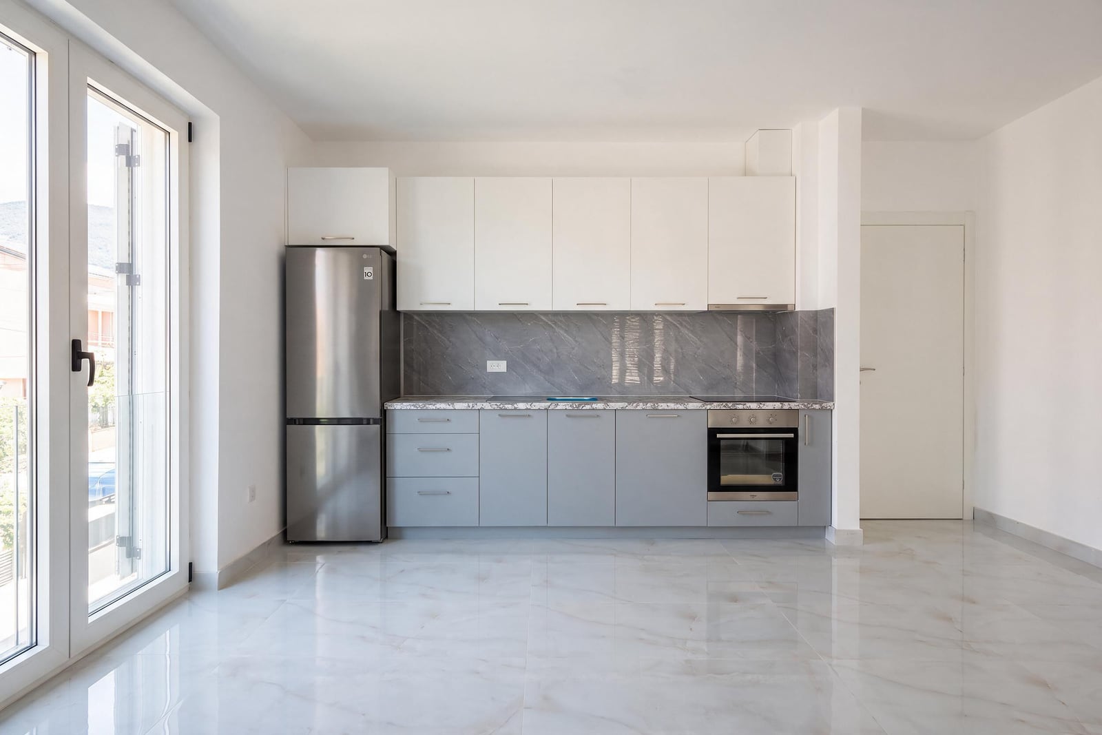 Modern kitchen in an apartment in Tivat, Montenegro: gray and white facades, built-in appliances, and marble flooring.