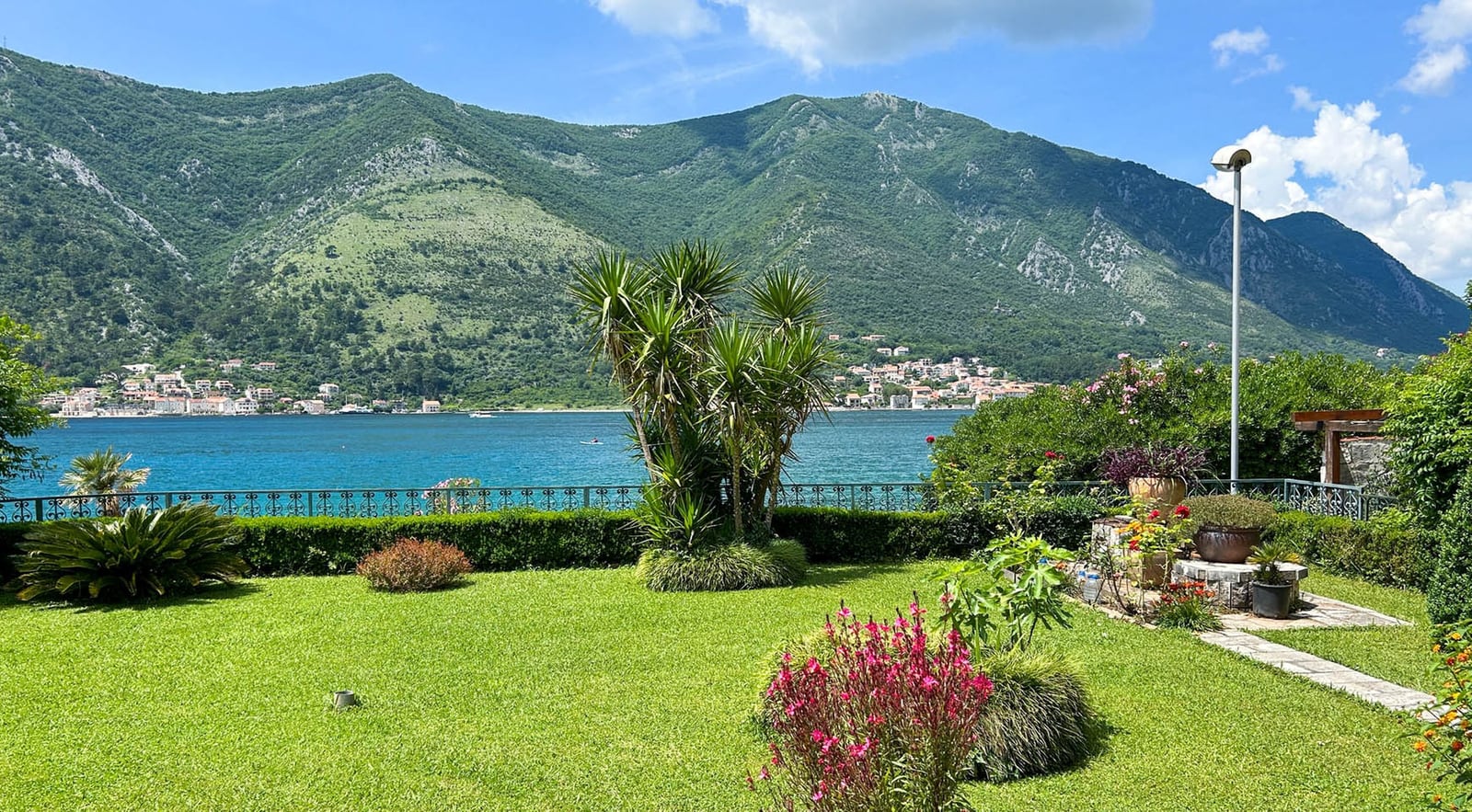 Grüner Garten der Villa in Dobrota, Montenegro, mit Panoramablick auf die Bucht von Kotor und die Berglandschaft.