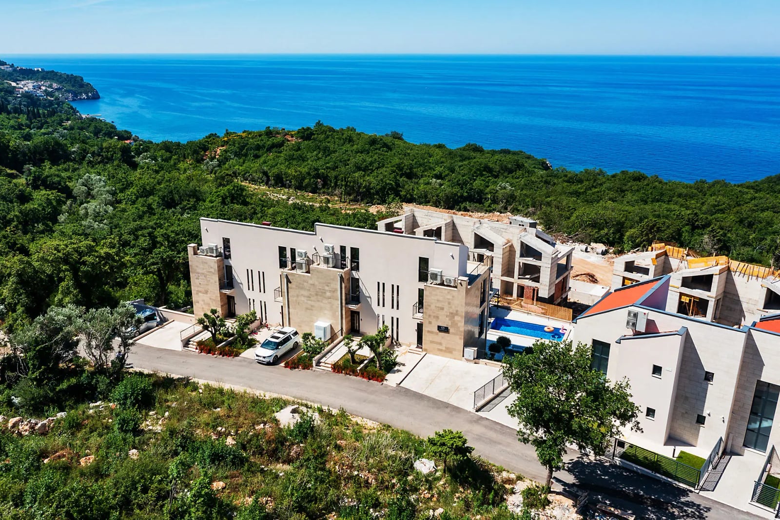 Modern villa with a swimming pool in Reževići, Montenegro: aerial view of the building complex by the sea, surrounded by greenery.