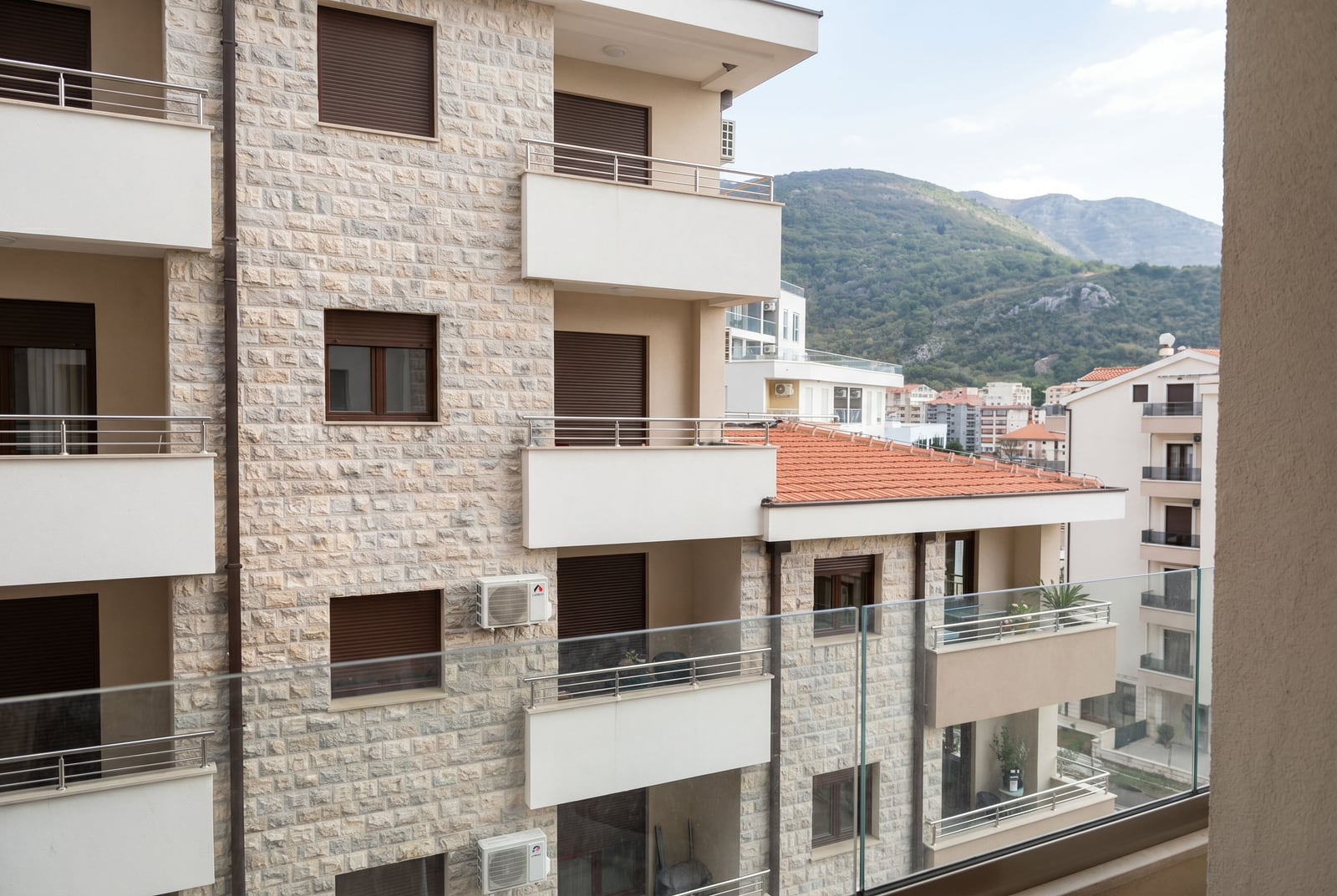 Steinfassade eines Wohnhauses mit Balkonen in Bečići, Montenegro, Blick auf benachbarte Gebäude und die Berge.
