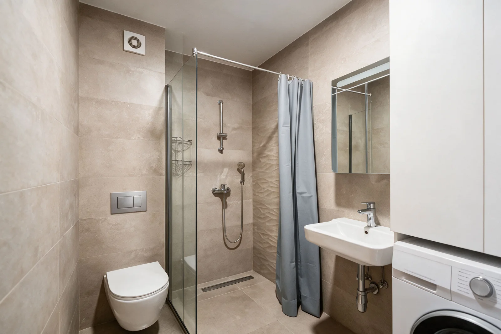Duş, duvar tipi tuvalet, lavabo ve çamaşır makinesi olan bej fayanslı banyo.