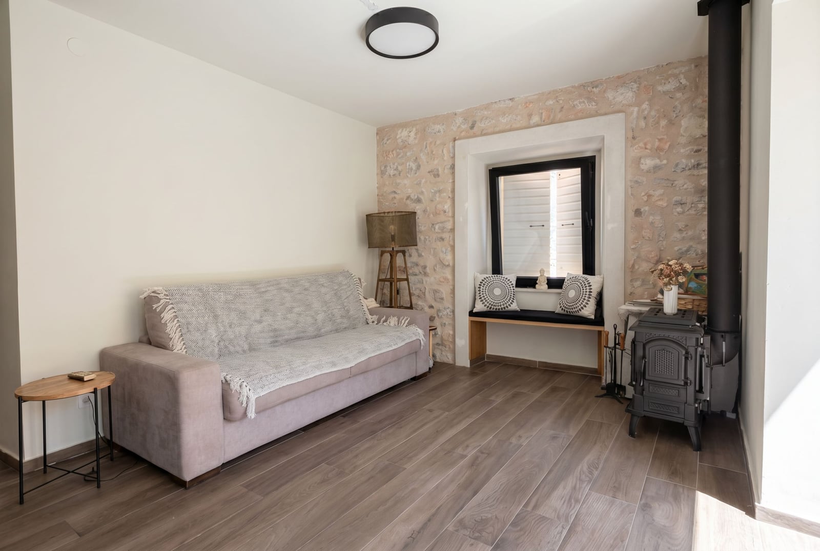 Living room in a house in Budva, Montenegro: a cozy sofa, stone wall, wood-burning stove, and a seating area by the window.
