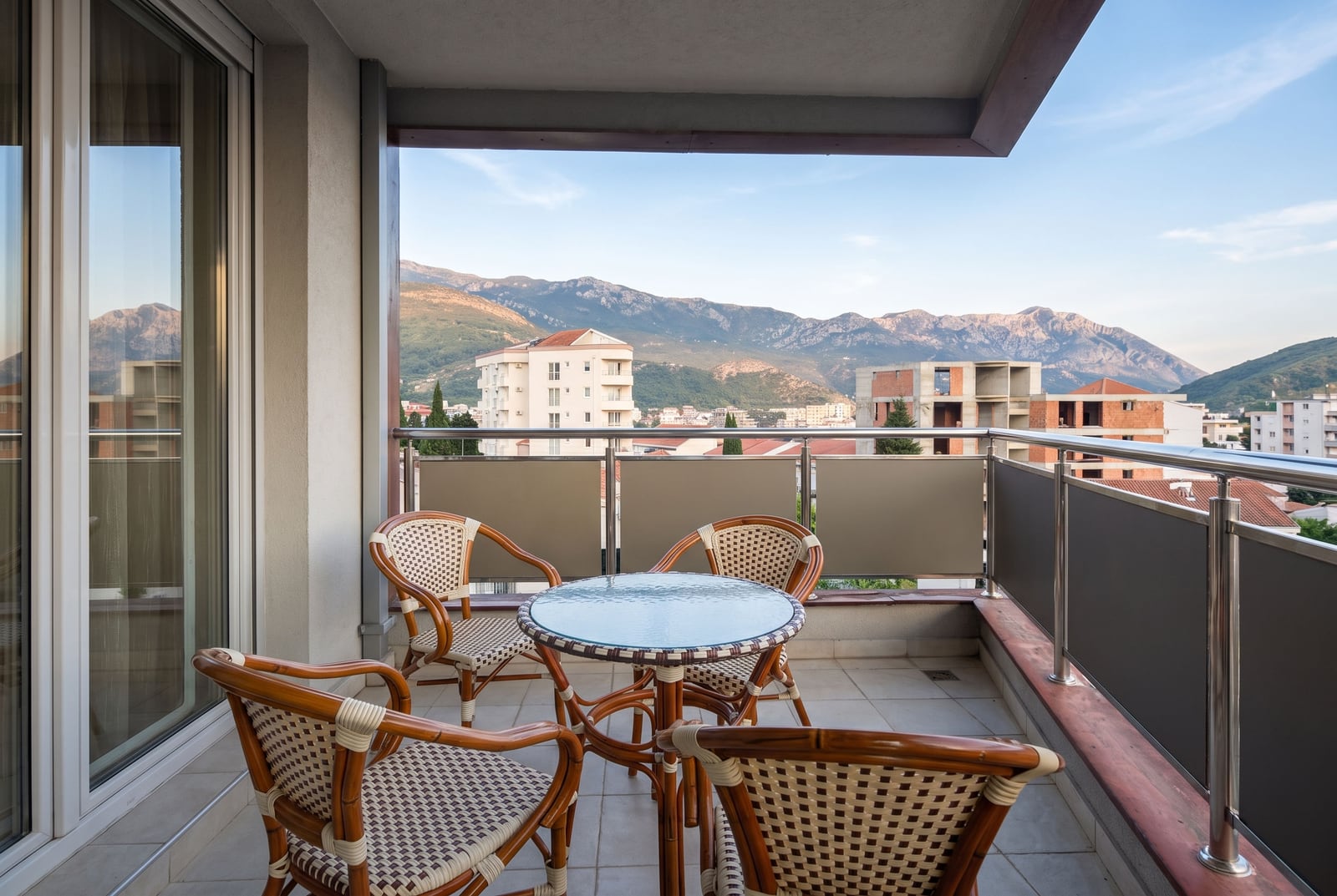 Spacious balcony with wicker furniture and panoramic mountain views in Bečići, Montenegro.
