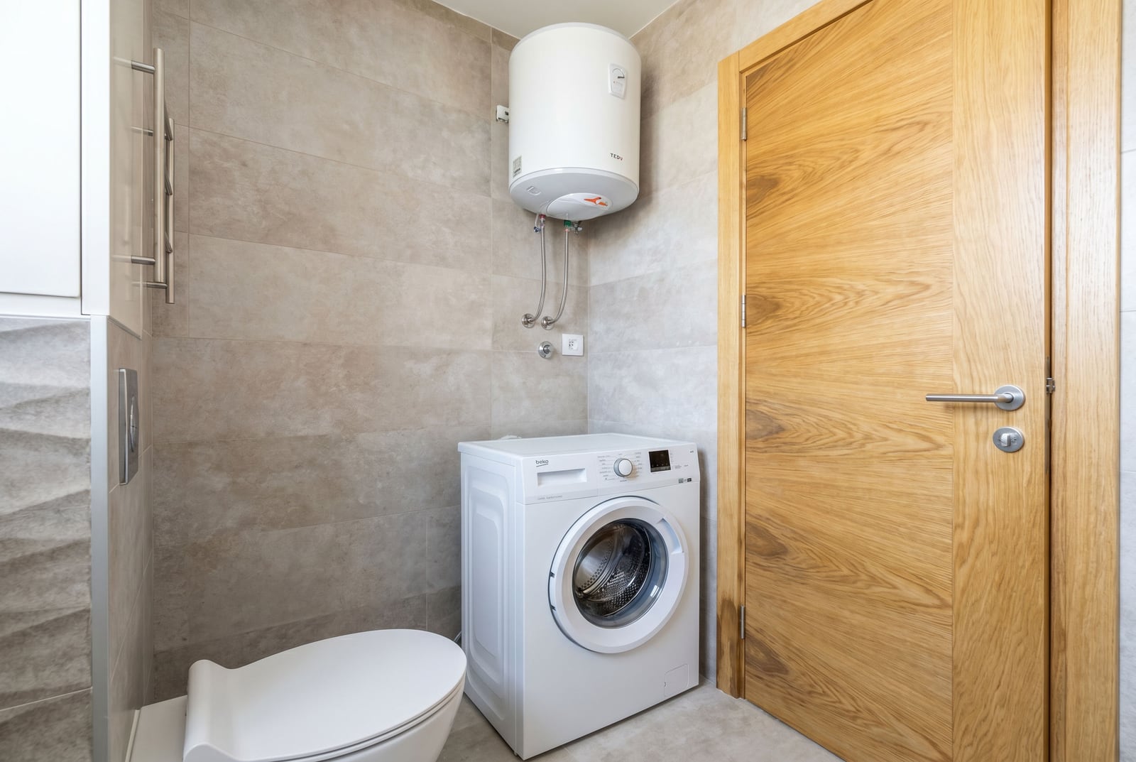 Badezimmer in einer Wohnung in Bečići, Montenegro: Waschmaschine, Boiler, moderne Fliesenoberflächen und Tür.
