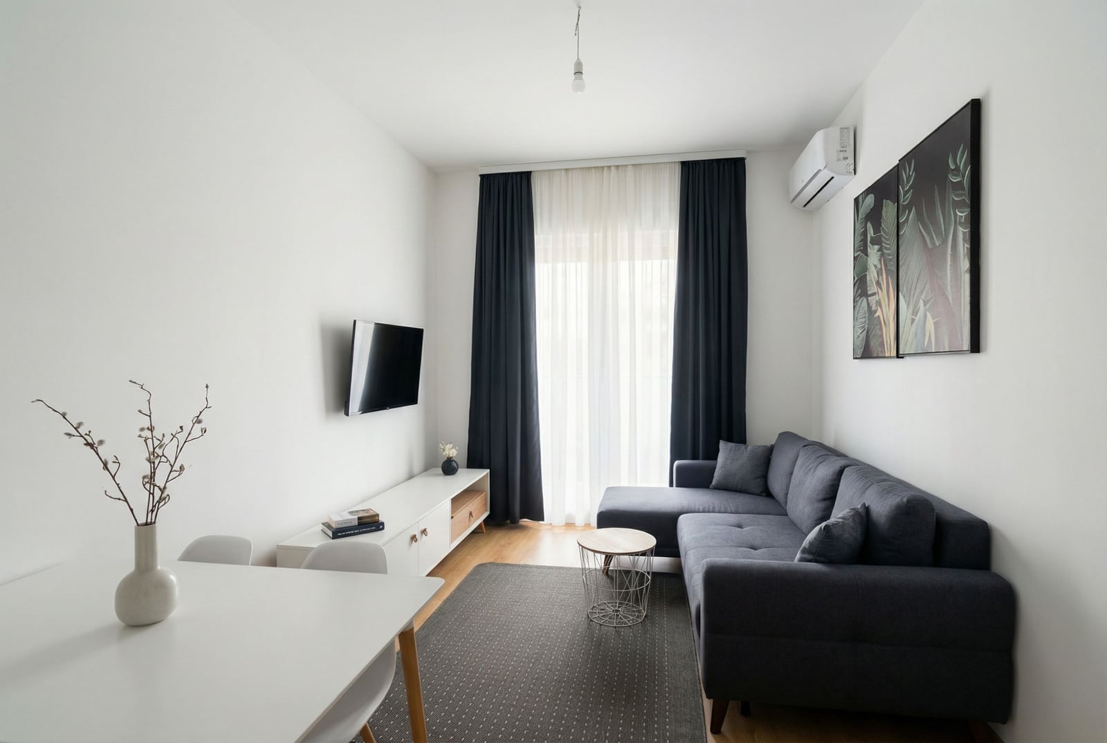 Savremena dnevna soba u stanu u Budvi, Crna Gora: siva sofa, beli nameštaj, TV i panoramski prozor sa zavesama.