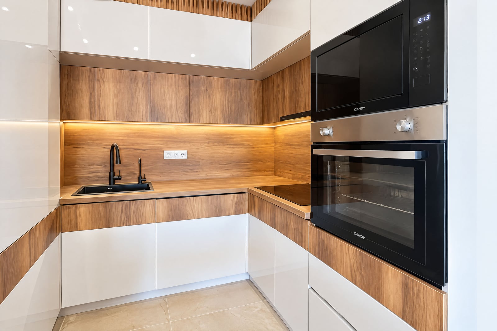 Modern kitchen with white and wood facades, built-in appliances, and lighting in an apartment in Budva, Montenegro