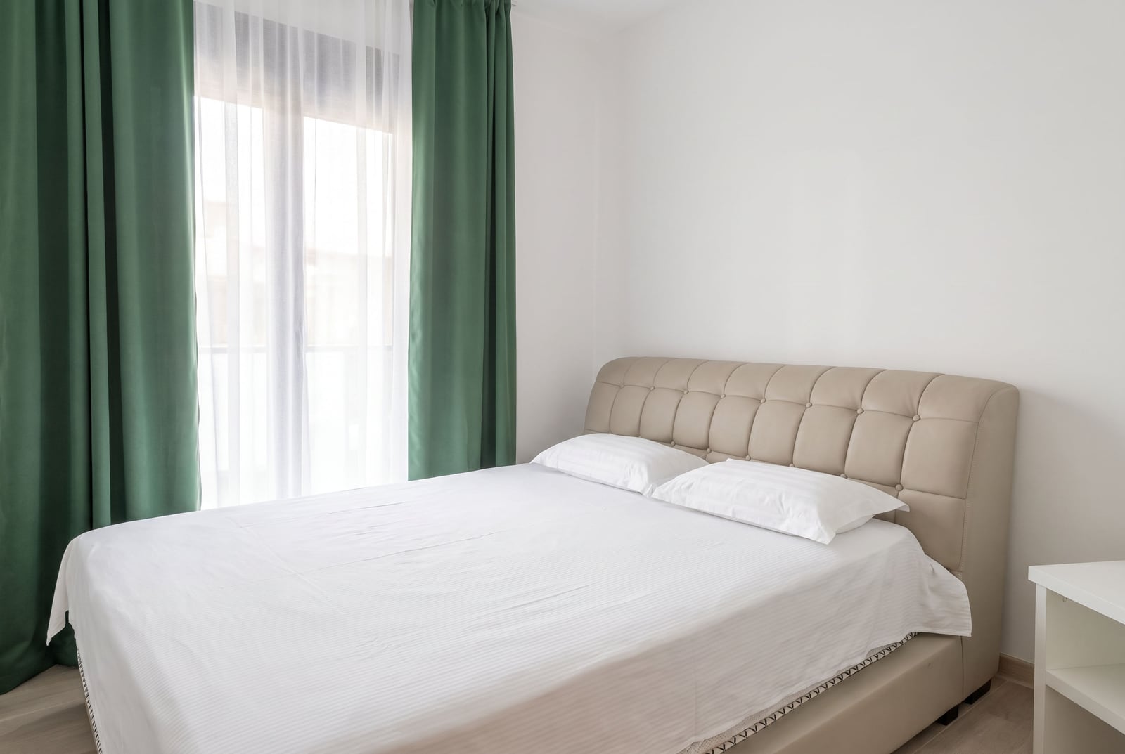 Helles Schlafzimmer mit beigem Doppelbett und grünen Vorhängen in einer Wohnung in Budva, Montenegro