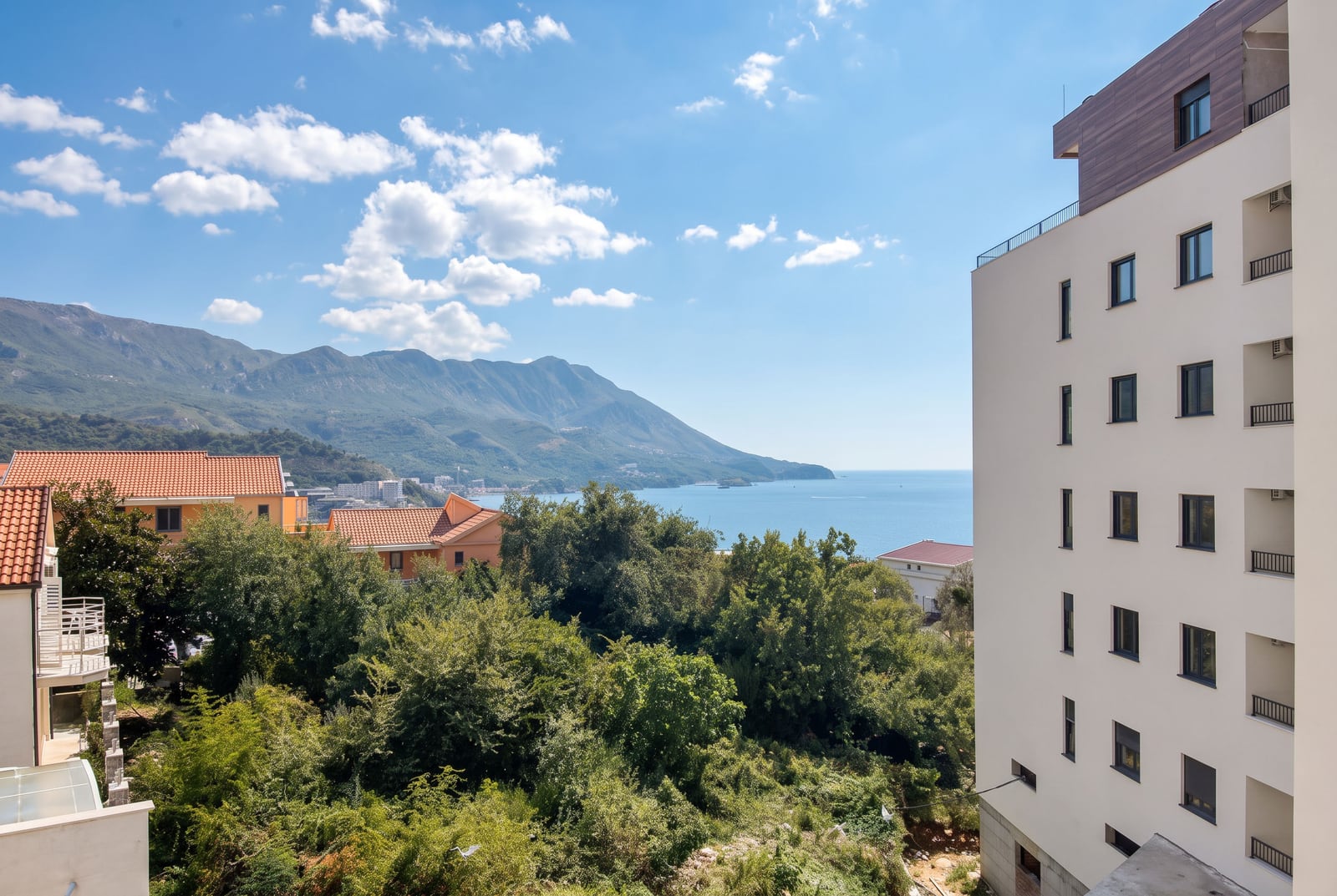 Panoramic view of the sea, mountains, and a modern residential complex in Becici, Montenegro