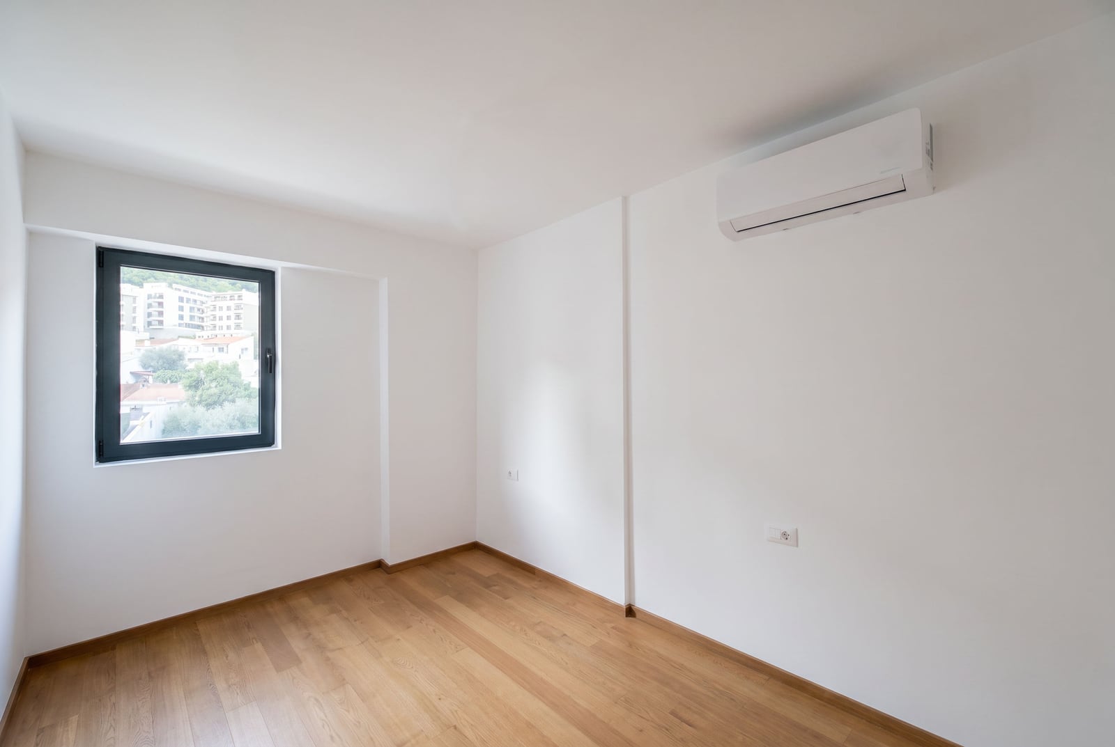 Bright bedroom with white walls, air conditioning, and parquet flooring in an apartment in Budva, Montenegro.