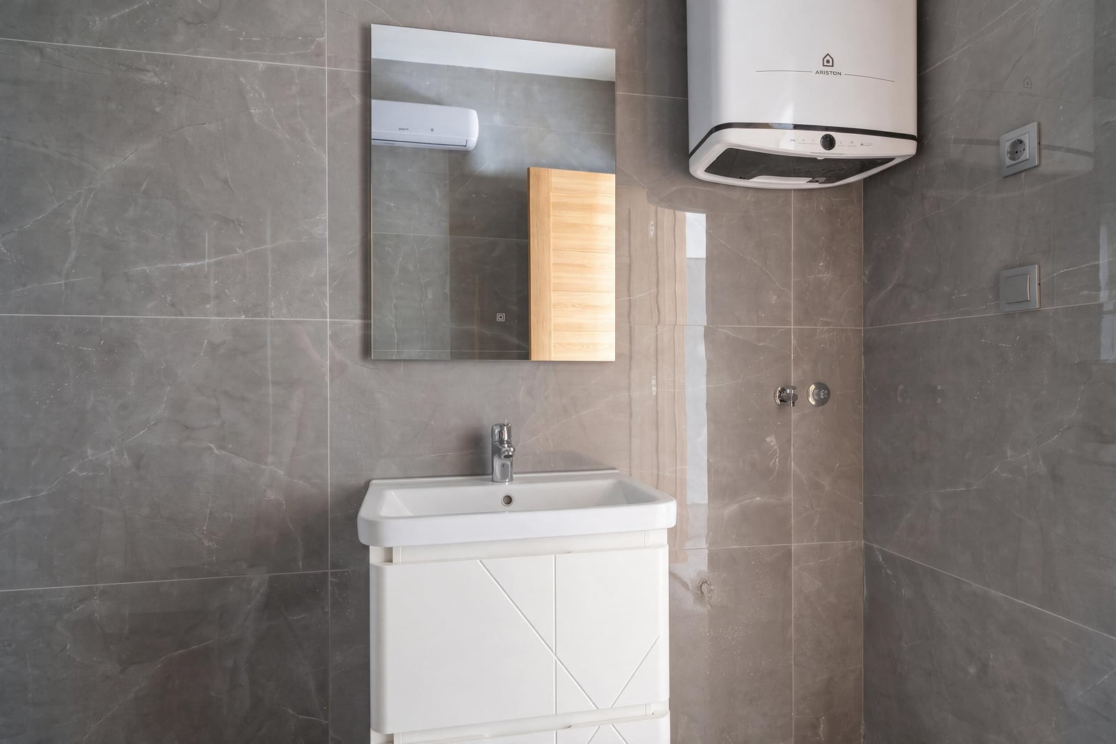 Modern bathroom in an apartment in Bar, Montenegro: gray tiles, white vanity with sink, and Ariston water heater.