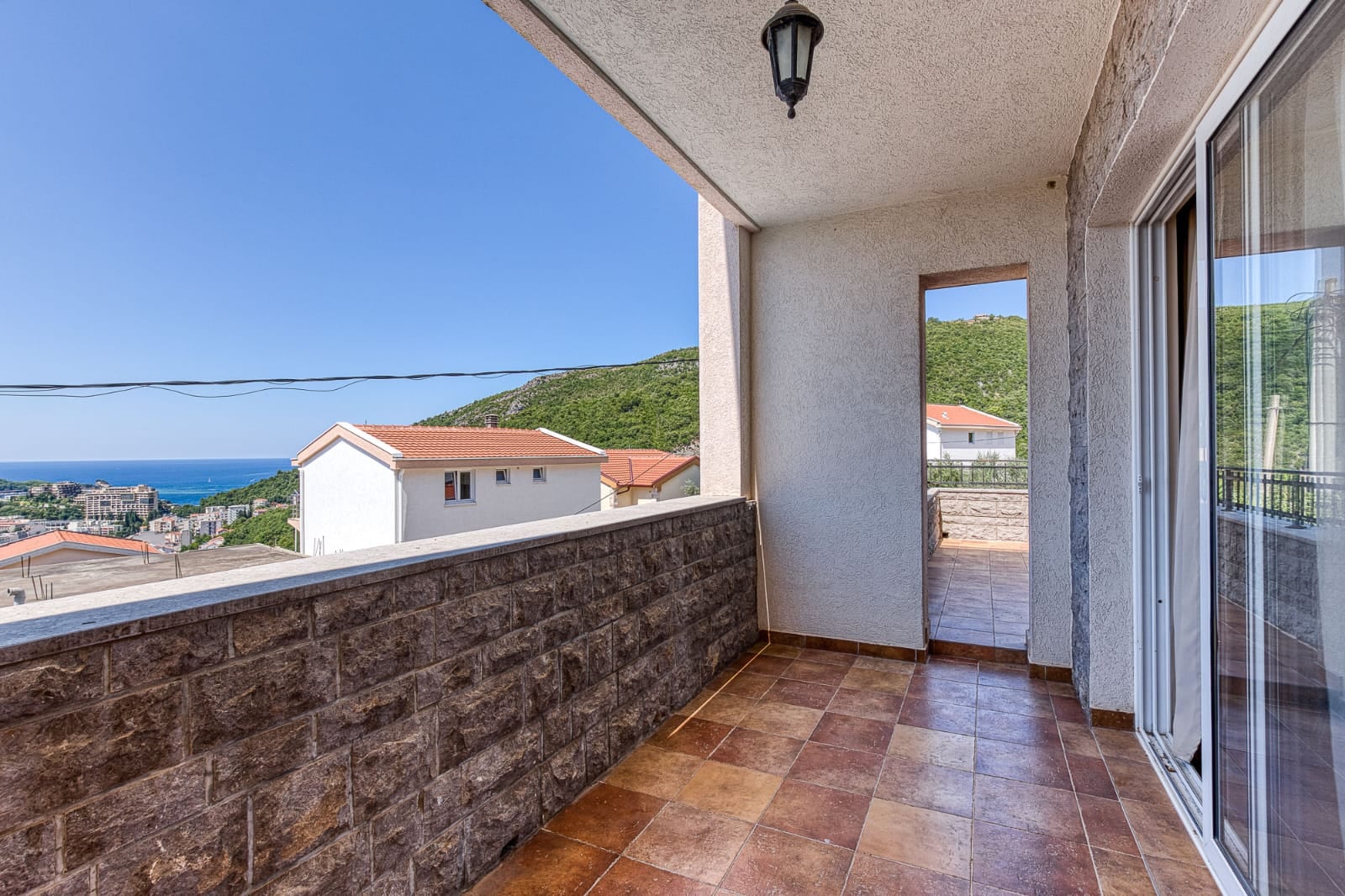 Balcon spacieux d'une villa à Bečići, Monténégro, avec finitions en pierre, carrelage et vue panoramique sur la mer et les montagnes.