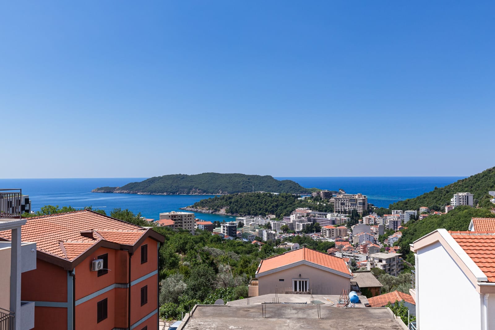 Vue panoramique sur la mer et la station balnéaire de Bečići, au Monténégro, depuis la terrasse d'une villa aux toits de tuiles entourée de verdure.