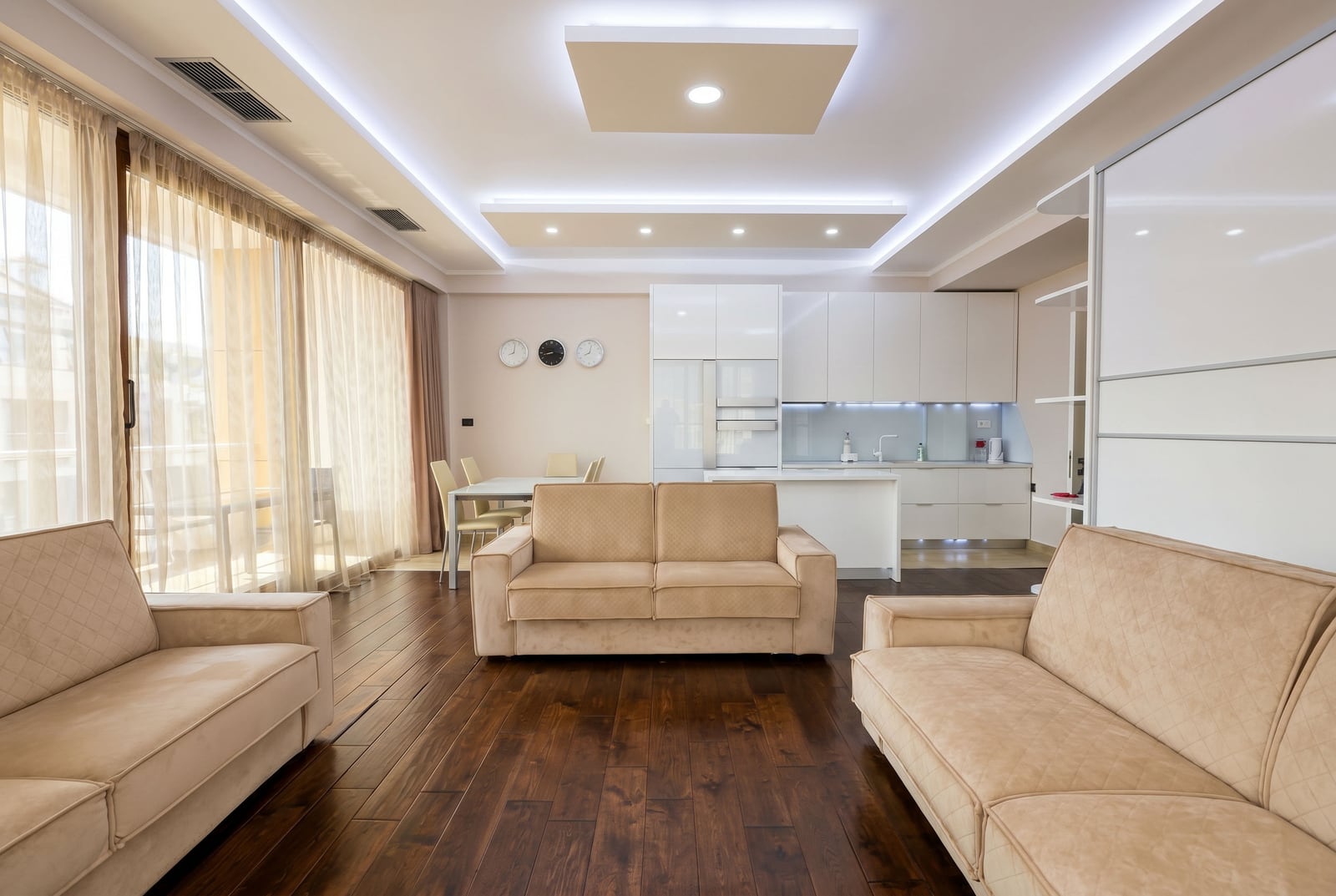 Modern living room with a white kitchen and beige sofas in an apartment in Budva, Montenegro. Panoramic windows and parquet flooring.