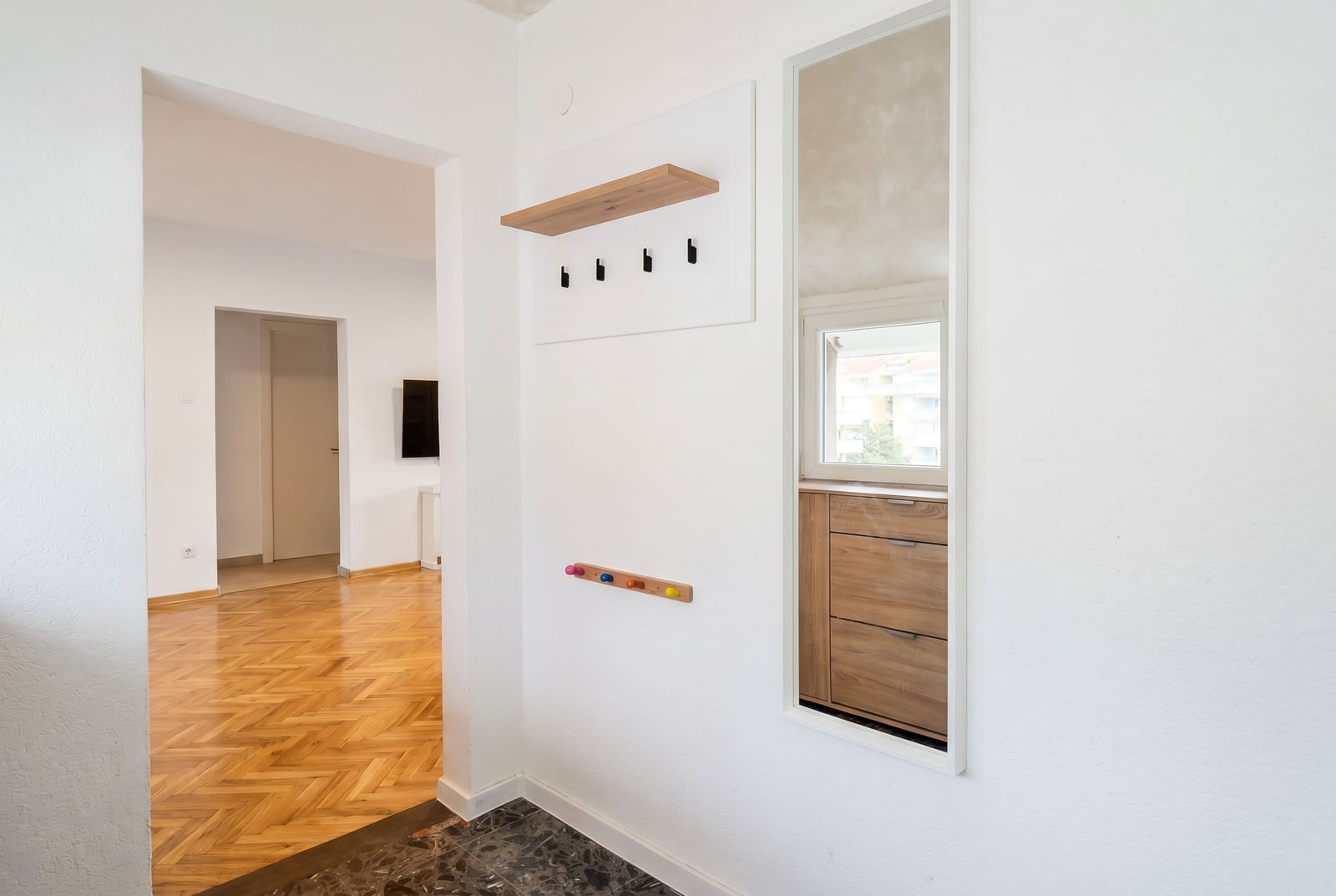 Bright hallway in an apartment in Budva, Montenegro: wall-mounted coat rack, mirror, and parquet flooring in the interior.