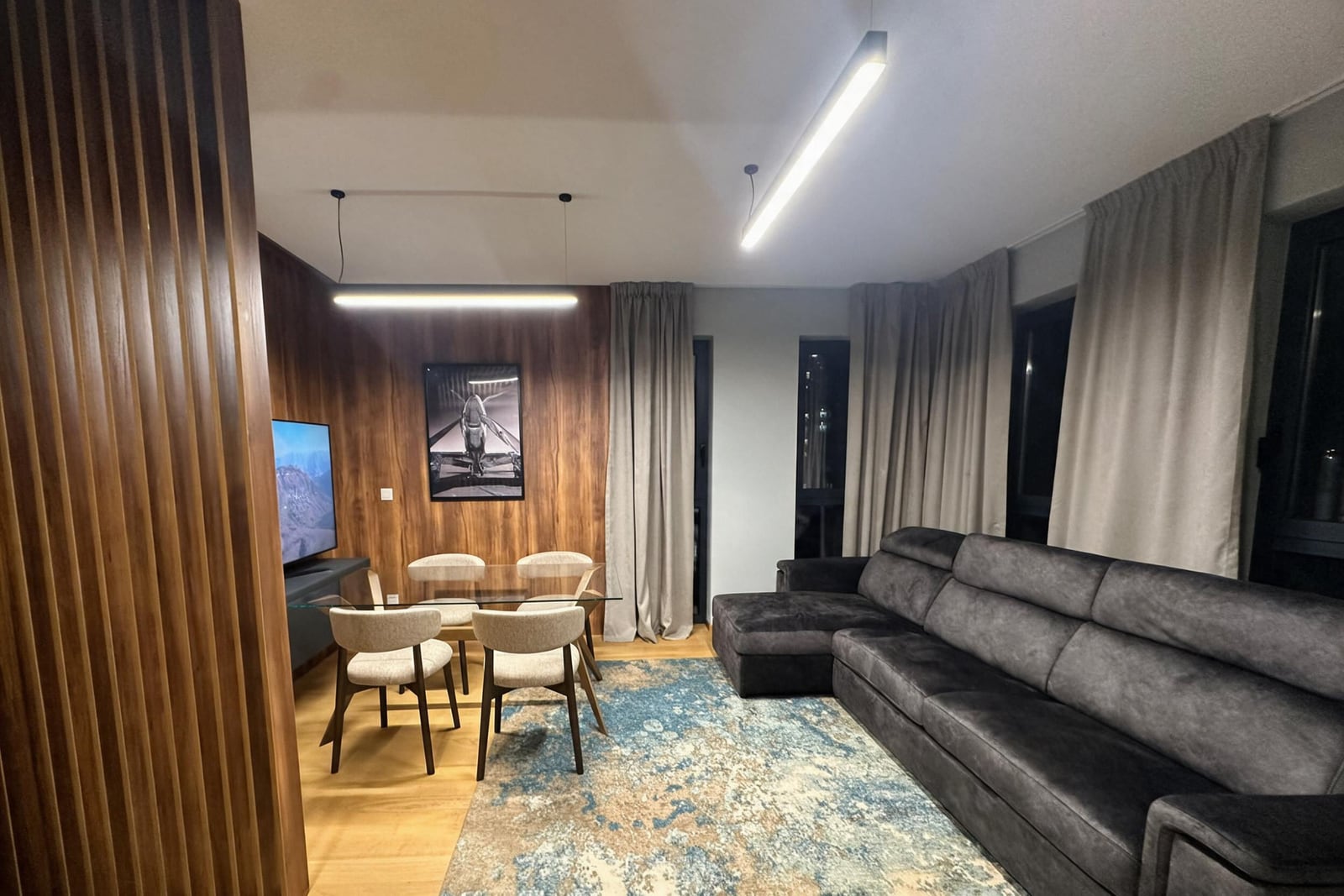 Modern living room with a soft corner sofa, dining area, and wooden wall paneling in an apartment in Budva, Montenegro.