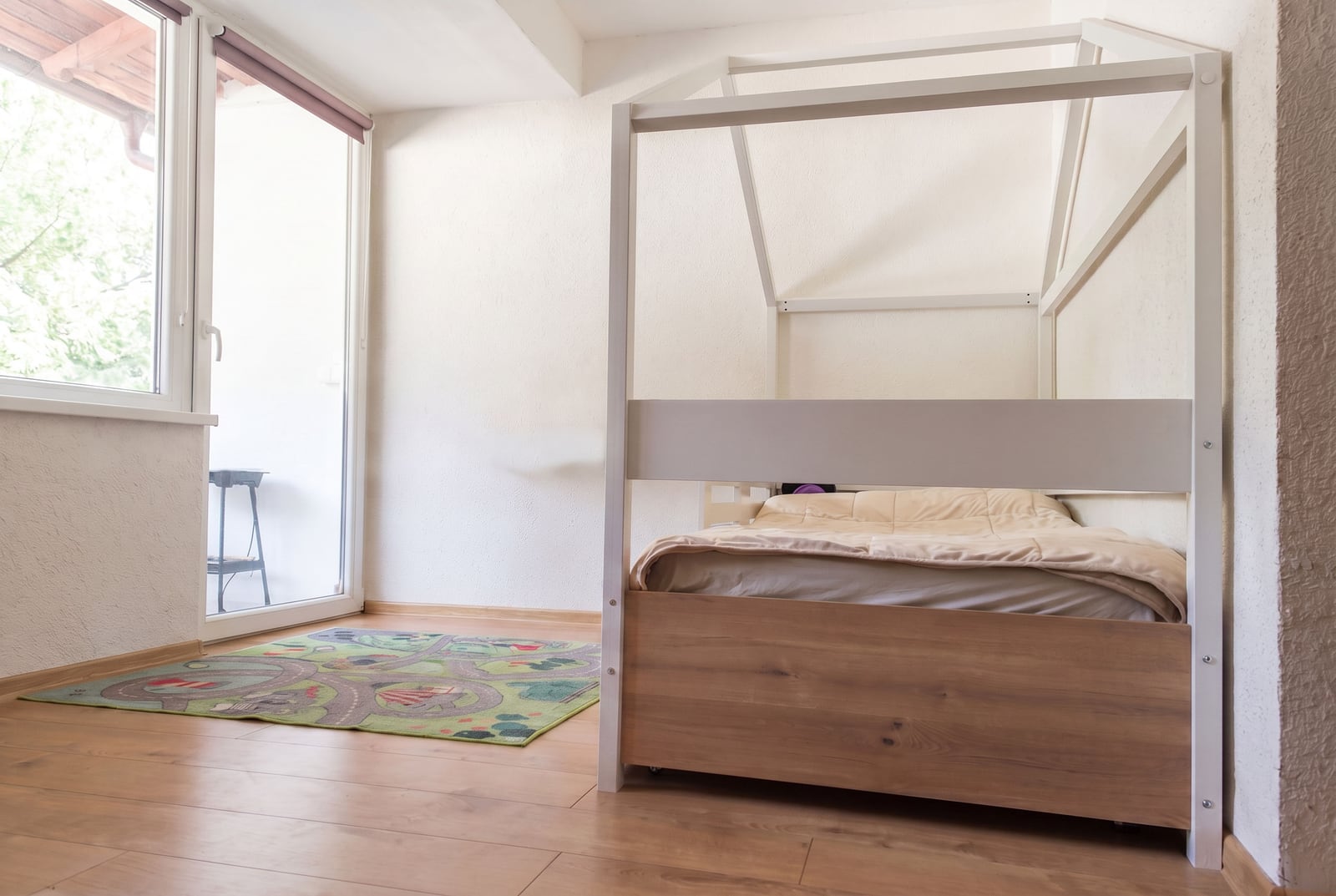 Children's bedroom with a house-shaped bed and a play mat in an apartment, Budva, Montenegro. Bright interior with access to a balcony.