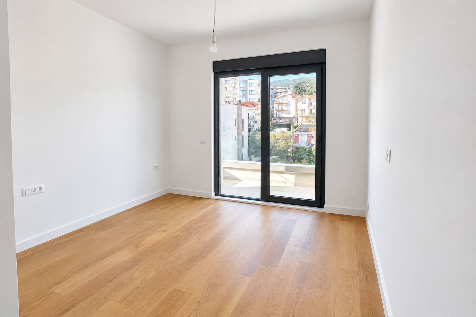 Chambre lumineuse et vide avec parquet et fenêtre panoramique sur la ville à Bečići, Monténégro