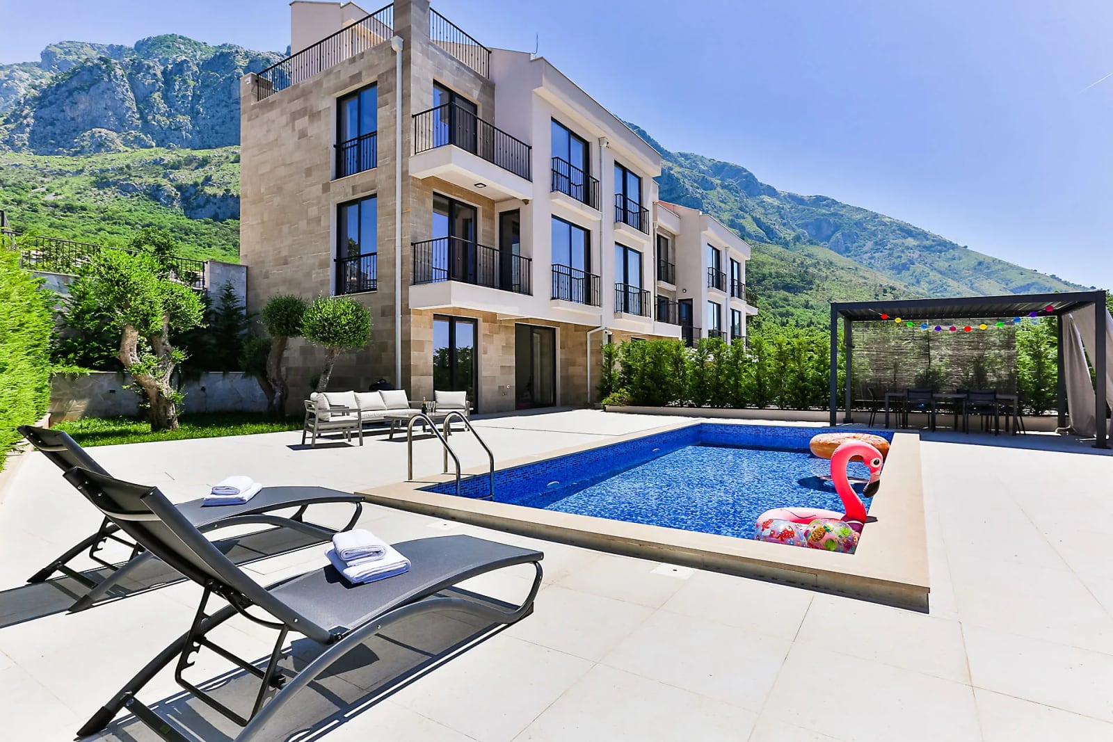 Villa moderne avec piscine et chaises longues à Reževići, Monténégro, avec des paysages montagneux pittoresques en arrière-plan.