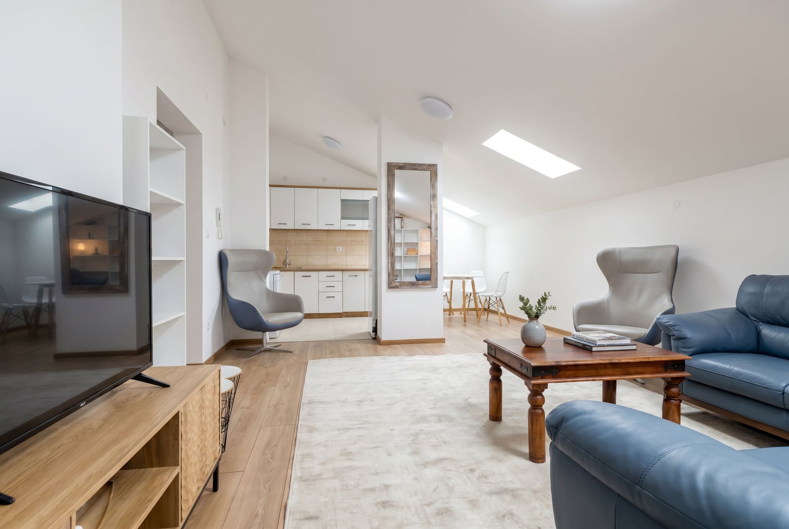 Modern living room with a kitchen in an attic apartment in Budva, Montenegro: blue leather sofa, armchairs, and bright interior.