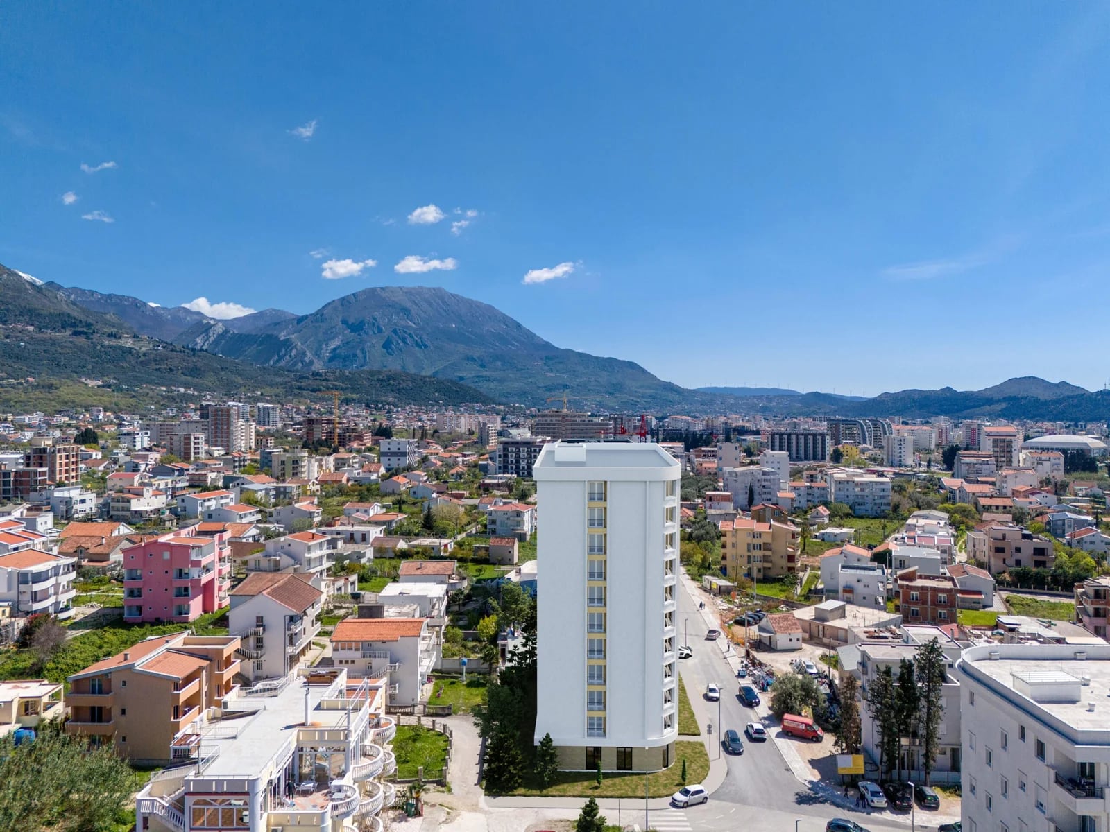 Blick aus der Höhe auf einen modernen Wohnkomplex in Bar, Montenegro, vor malerischer Bergkulisse.
