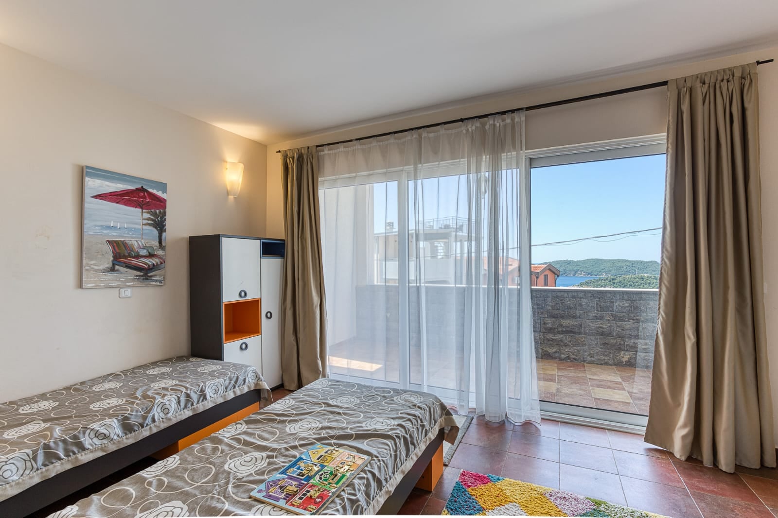 Chambre avec deux lits et accès à une terrasse avec vue sur la mer dans une villa à Bečići, au Monténégro.