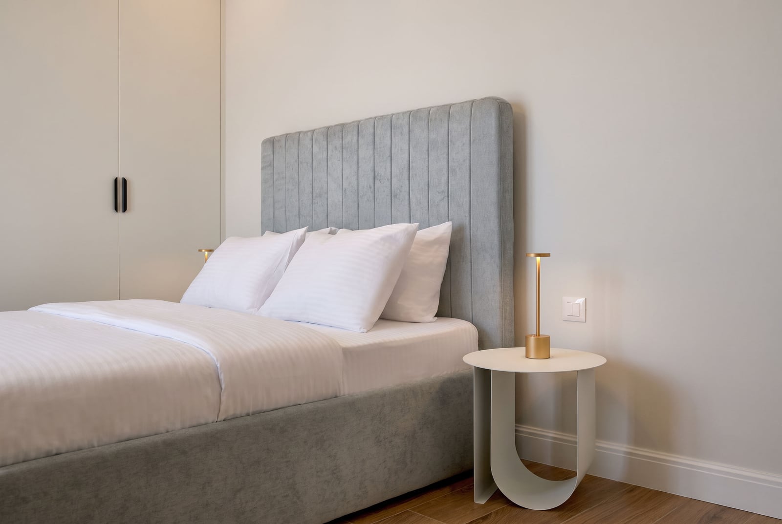Modernes Schlafzimmer mit einem weichen grauen Bett, einem weißen Schrank und einem Nachttisch in einer Wohnung in Luštica, Montenegro