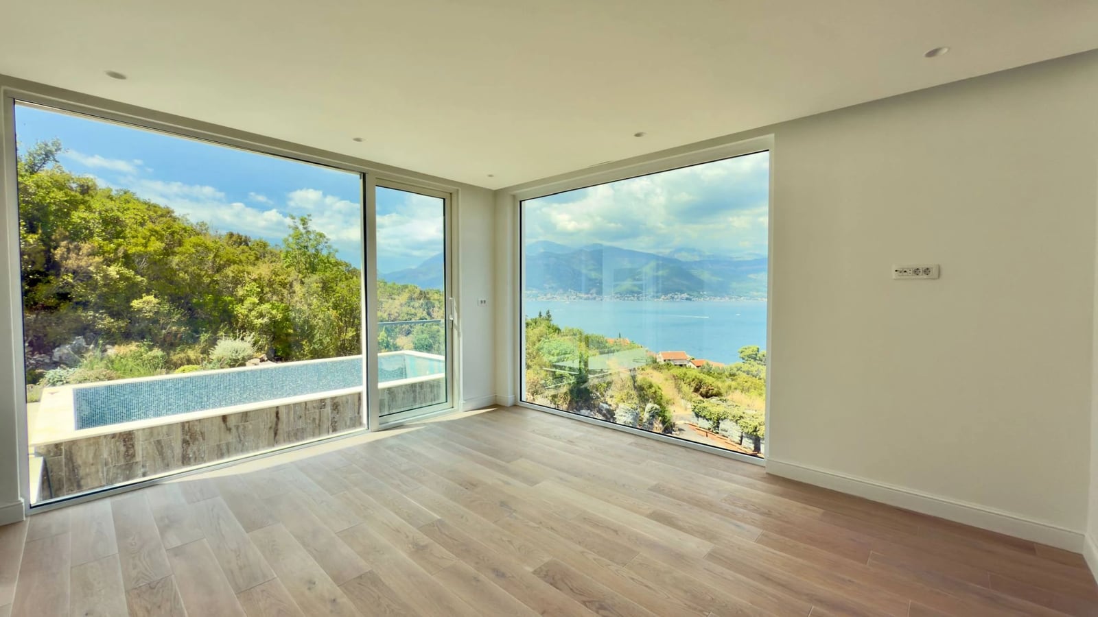 Wohnzimmer mit Panoramafenstern, Meerblick und Pool in einer Villa in Krašići, Montenegro. Helles Interieur mit Parkett.