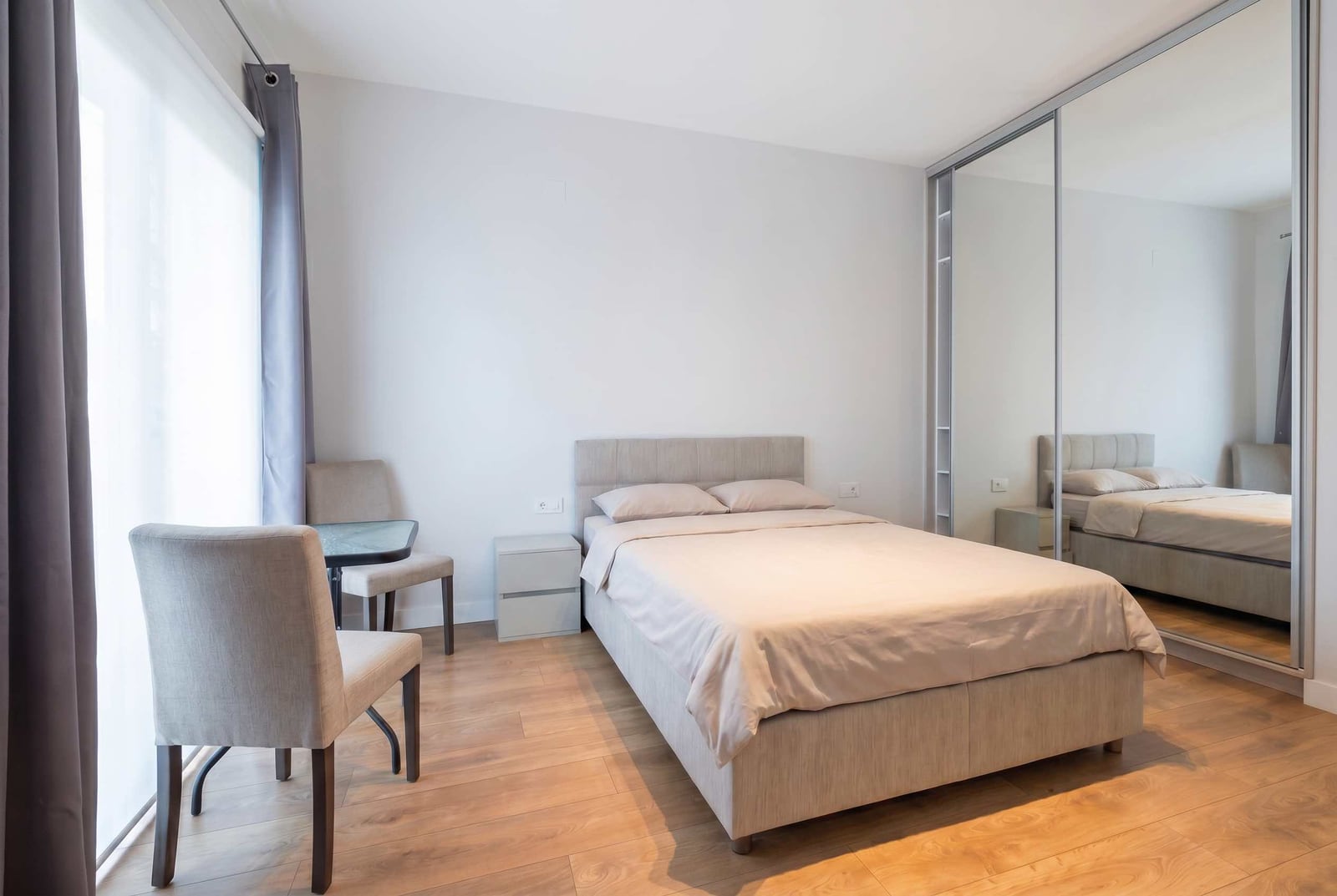 Helles Schlafzimmer in einer Wohnung, Kavač, Montenegro: Doppelbett, Spiegel-Kleiderschrank und Tisch mit Stühlen.