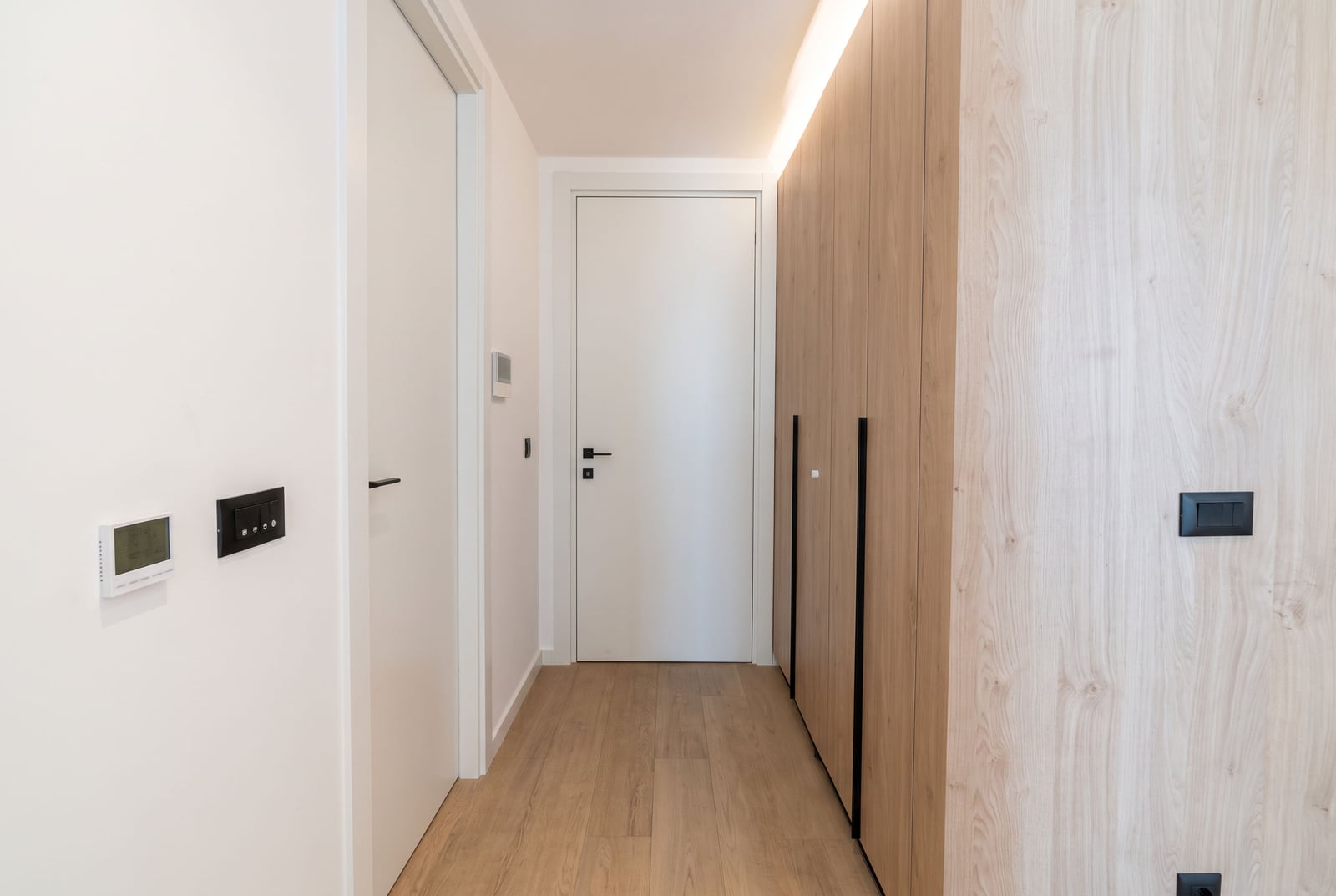Modern bright hallway with a wooden wardrobe, white interior doors, and laminate flooring in an apartment in Budva, Montenegro.
