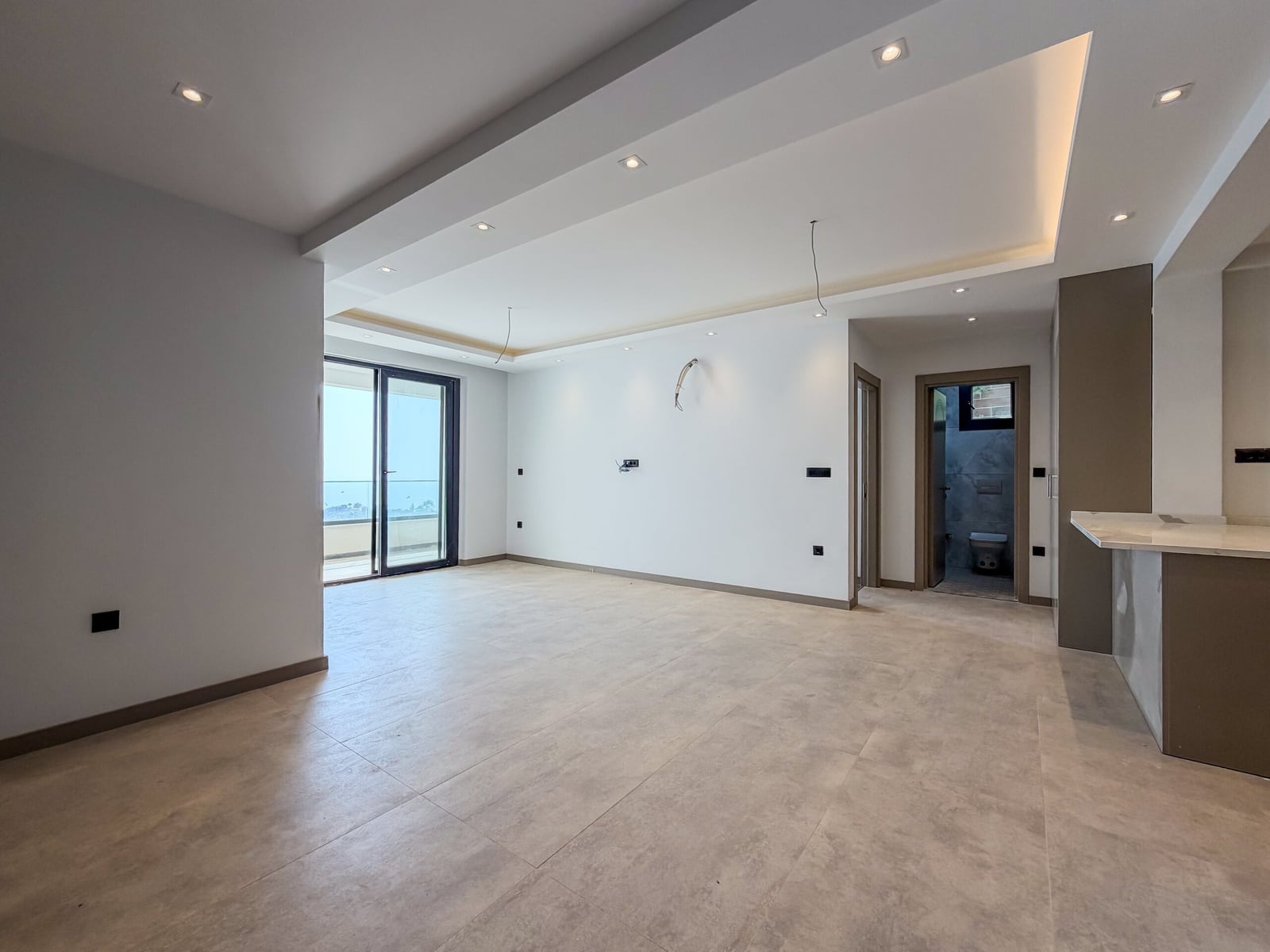 Spacious living room with finished interior, floor tiles, and a panoramic window in a new apartment in Budva, Montenegro