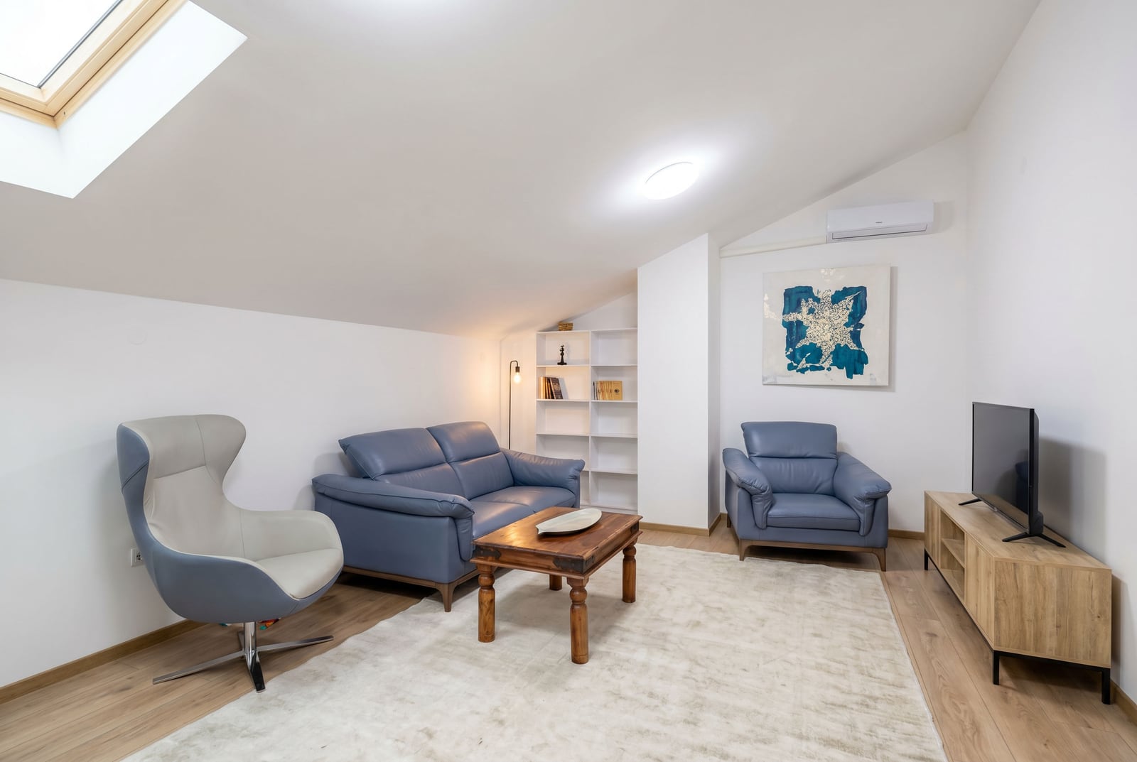 Bright living room in an attic apartment in Budva, Montenegro: leather furniture, wooden coffee table, and skylight.