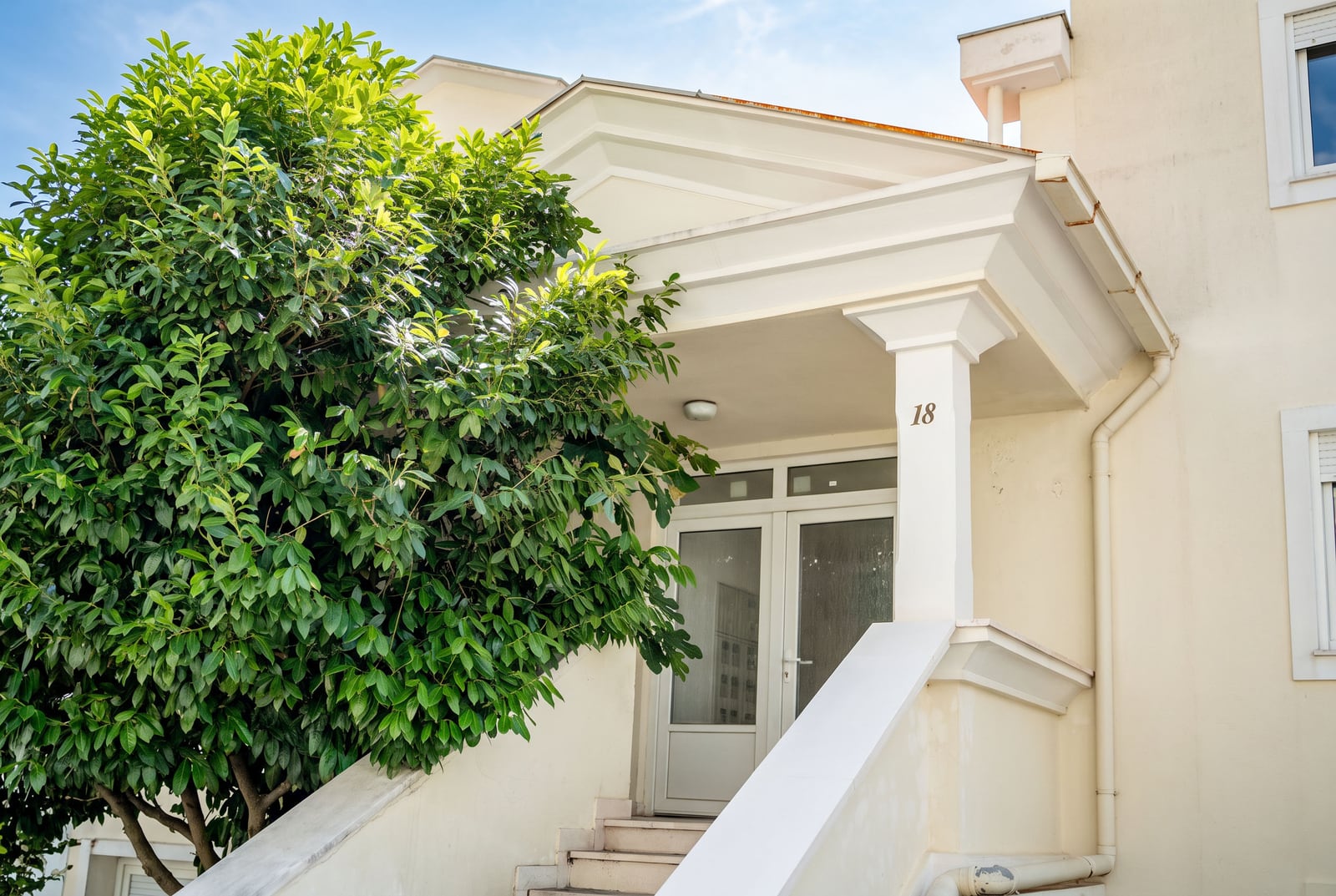 Entrance to the house with a white staircase and a green tree, property in Sveti Stefan, Montenegro.