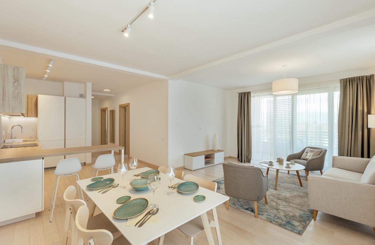 Modernes Wohnzimmer mit Küche in einem Apartment in Igalo, Montenegro: Essbereich, helle Möbel und Panoramafenster.