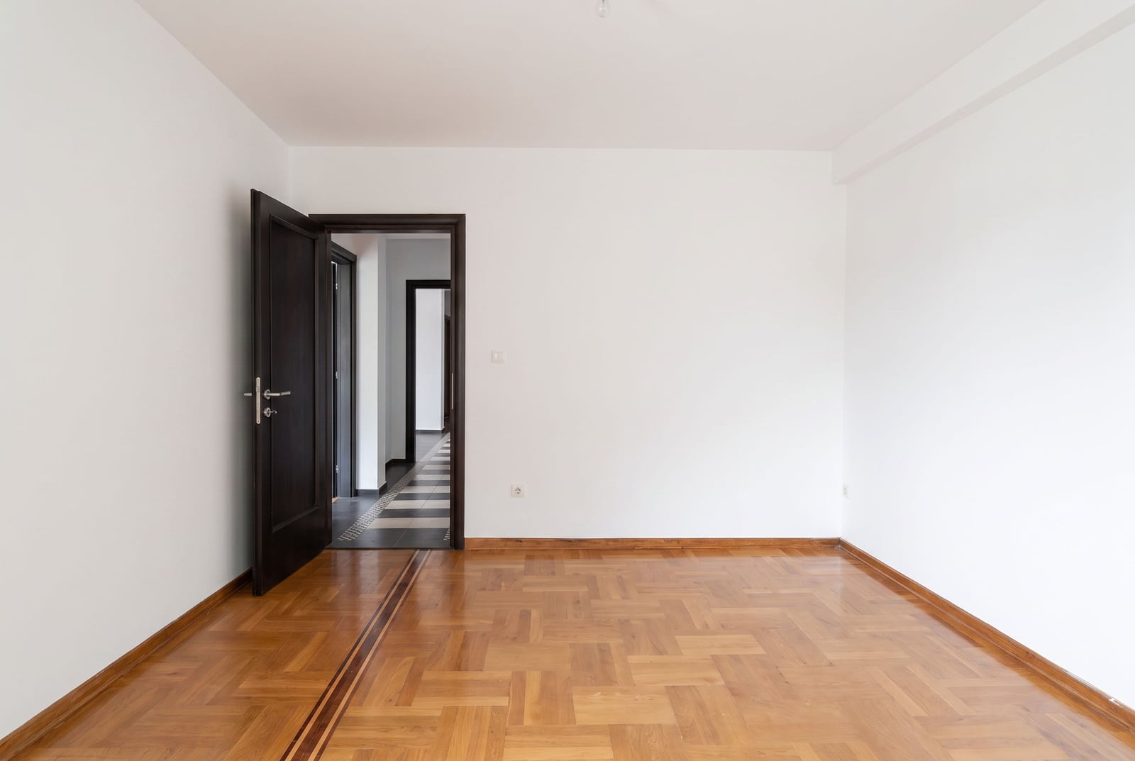 Empty bedroom with white walls, parquet flooring, and a dark interior door in an apartment in Petrovac, Montenegro.