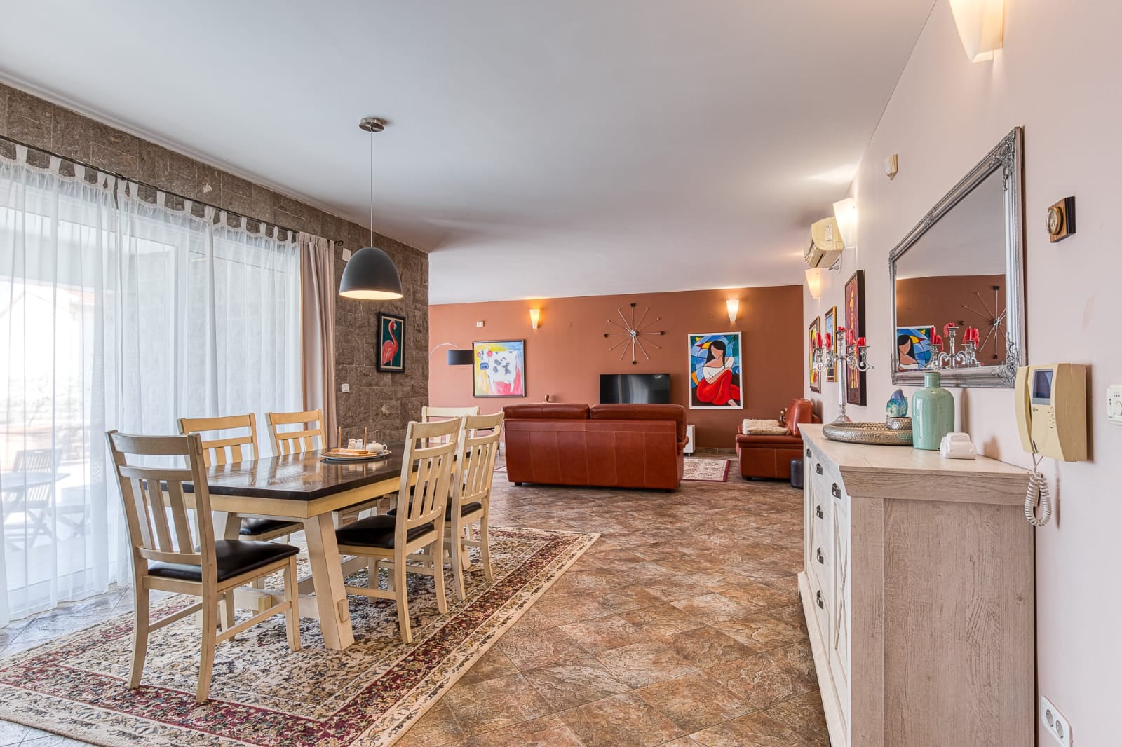 Salon spacieux avec coin repas dans une villa à Bečići, Monténégro : mobilier en cuir, finitions en pierre et baies vitrées.