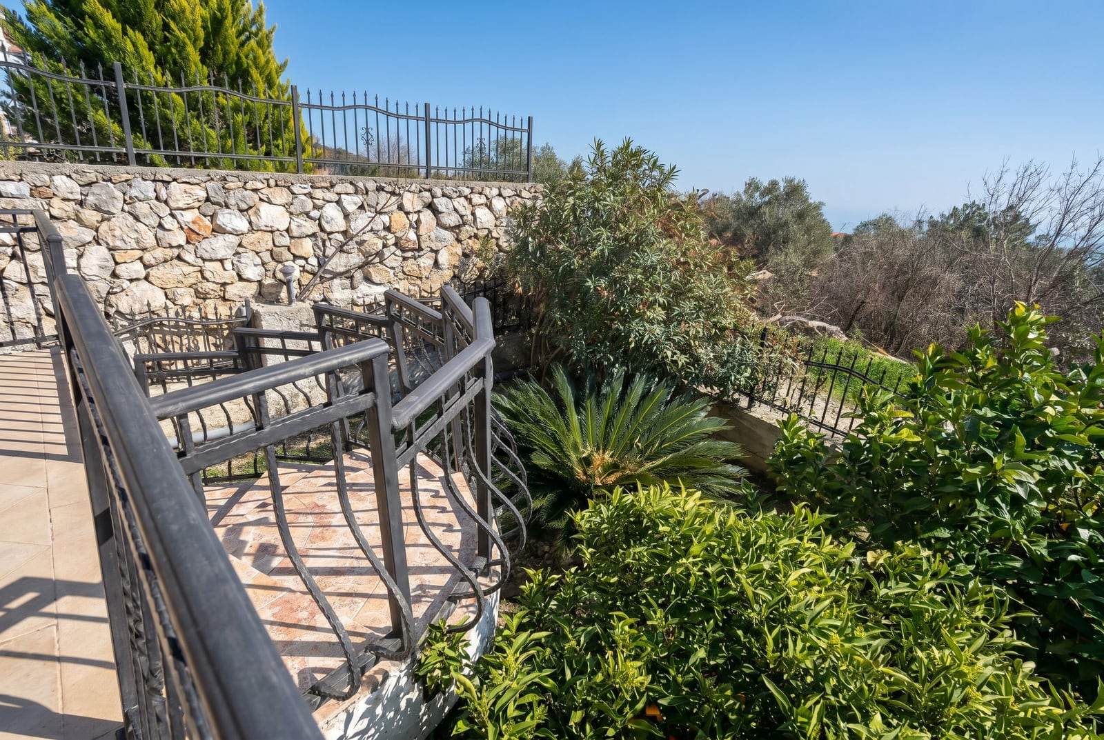 Balcony with a wrought-iron railing and a stone wall in a house, Buljarica, Montenegro, overlooking the garden and Mediterranean nature.