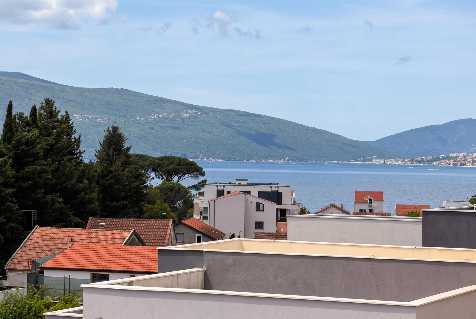 Panoramic view of the sea, mountains, and tiled rooftops of Tivat from the balcony of an apartment in Montenegro.