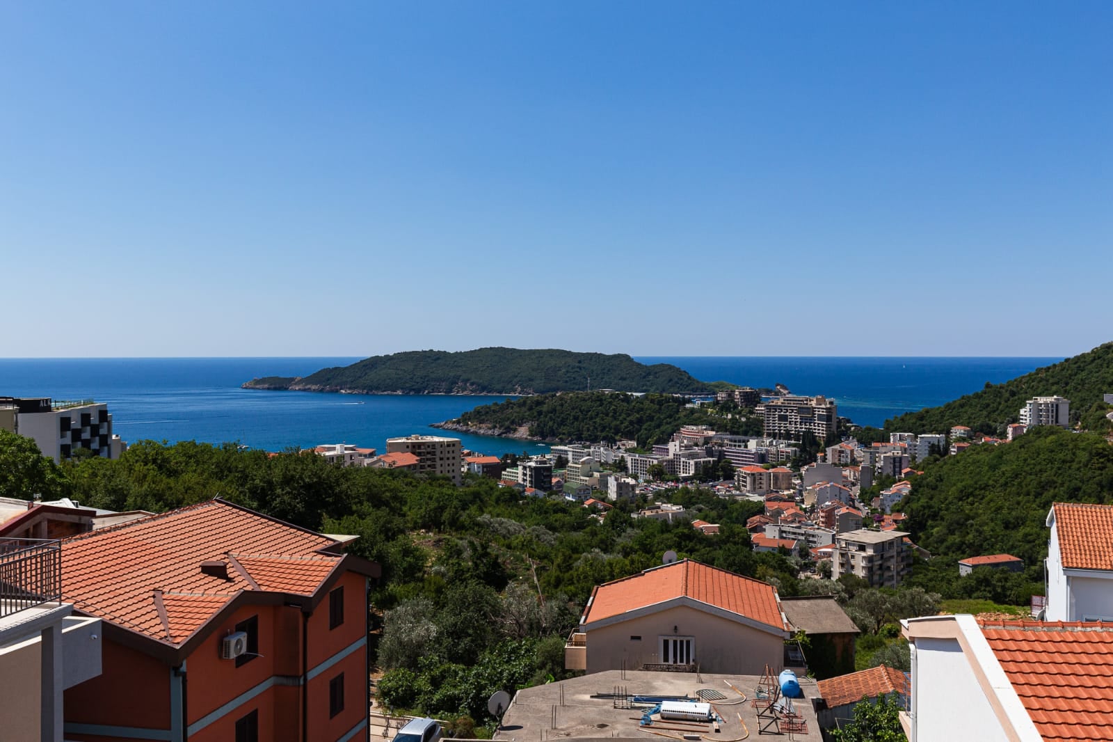 Vue panoramique sur la mer et l'île Saint-Nicolas depuis une villa à Bečići, au Monténégro : zones urbaines et collines verdoyantes.