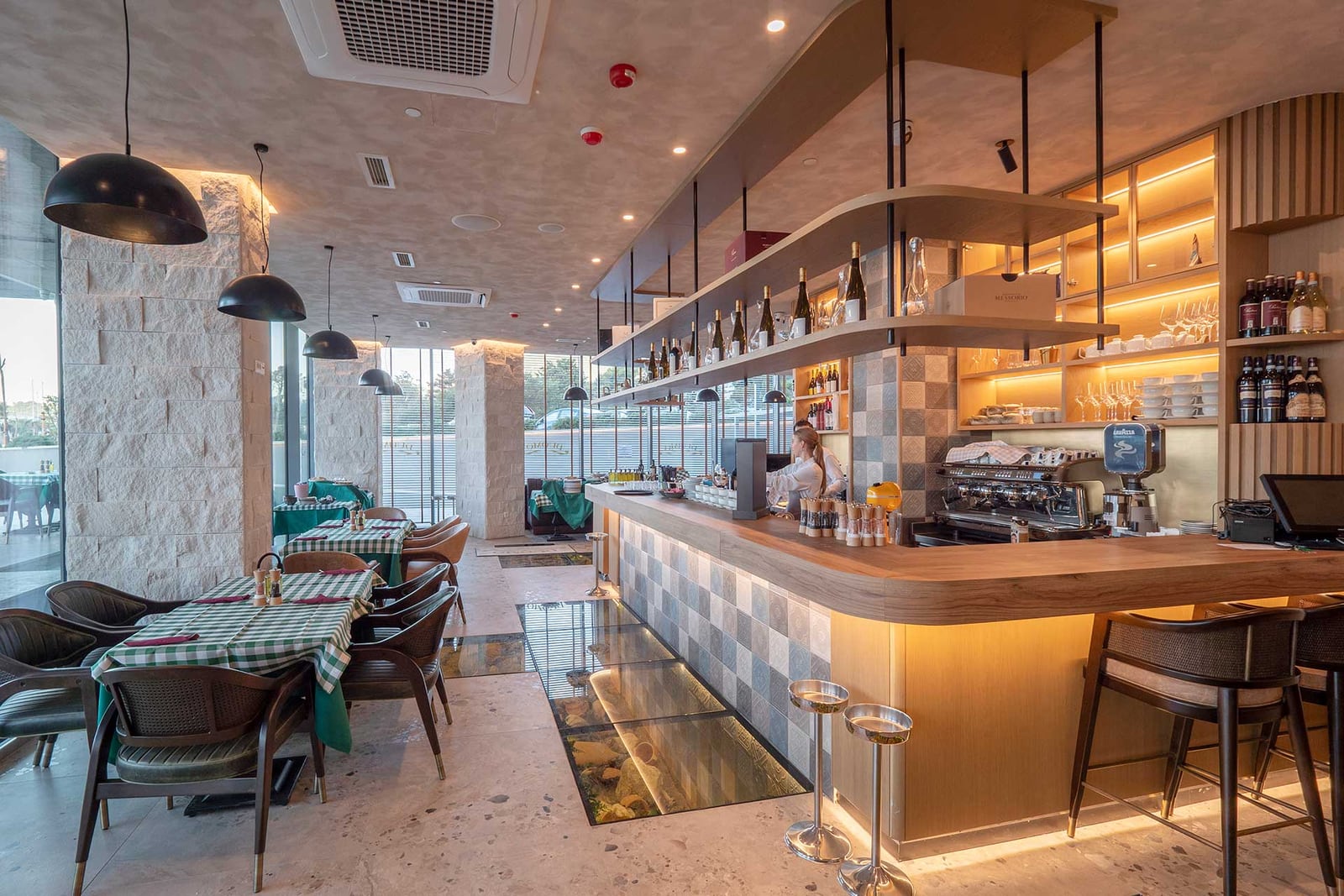 Interijer modernog restorana sa drvenim barskim pultom, stolovima u Bečićima, Crna Gora
