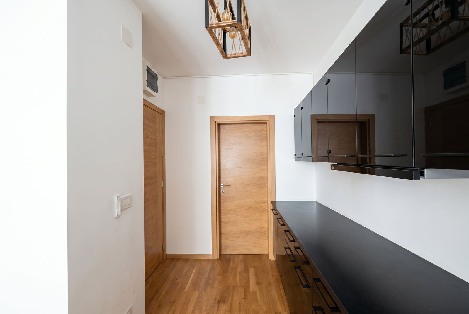 Moderne Küche mit schwarzen Hochglanzfronten in einer Wohnung in Bečići, Montenegro: stilvolles Interieur und Holztüren.