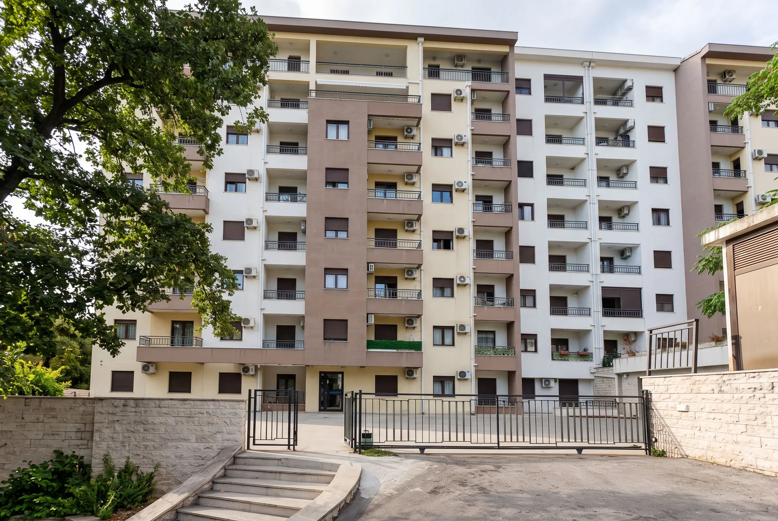 View of a multi-story residential building with balconies, AC units, and a metal gate in the foreground.