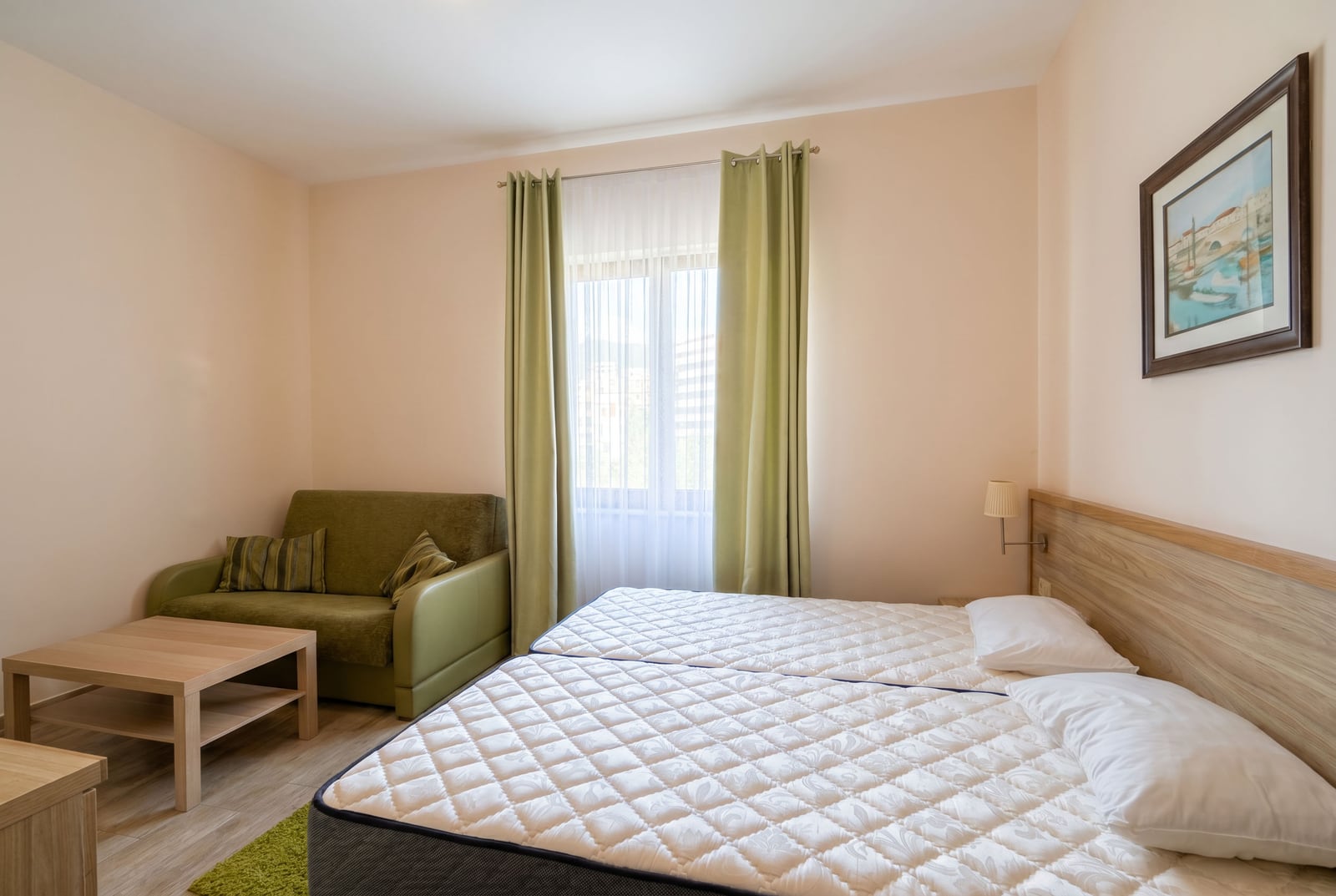 Bright bedroom in an apartment in Rafailovici, Montenegro: double bed, green sofa, and wooden coffee table.
