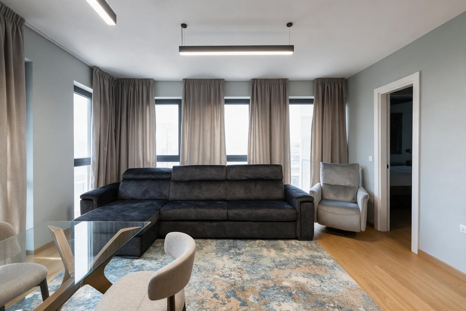 Modern living room with a dark corner sofa, panoramic windows, and a glass table in an apartment in Budva, Montenegro.