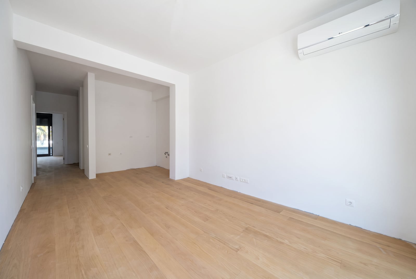 Empty living room with white walls, parquet flooring, and air conditioning in an apartment in Becici, Montenegro
