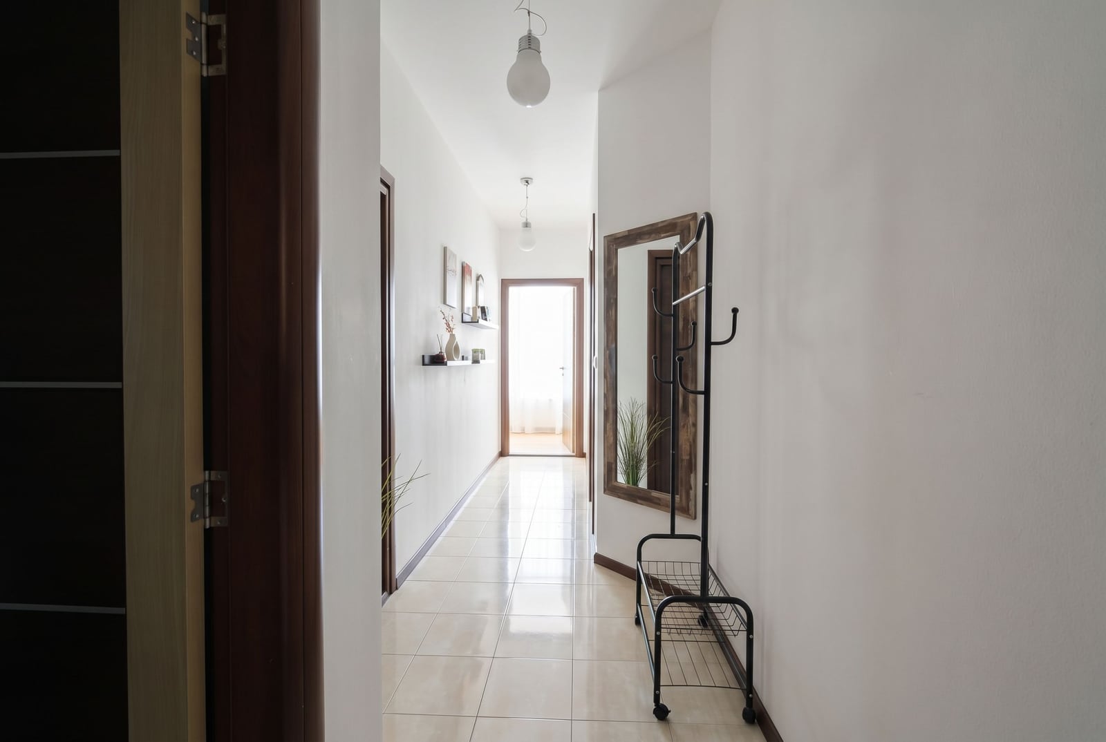 Svetao hodnik u stanu u Budvi, Crna Gora: pločice na podu, ogledalo u ramu, vešalica i izlaz na balkon.