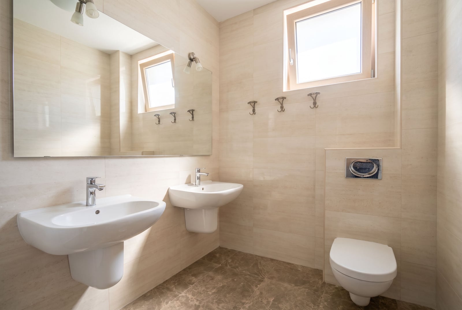 Modern bathroom in an apartment in Bečići, Montenegro: white fixtures, two sinks, wall-hung toilet, and beige finishes...
