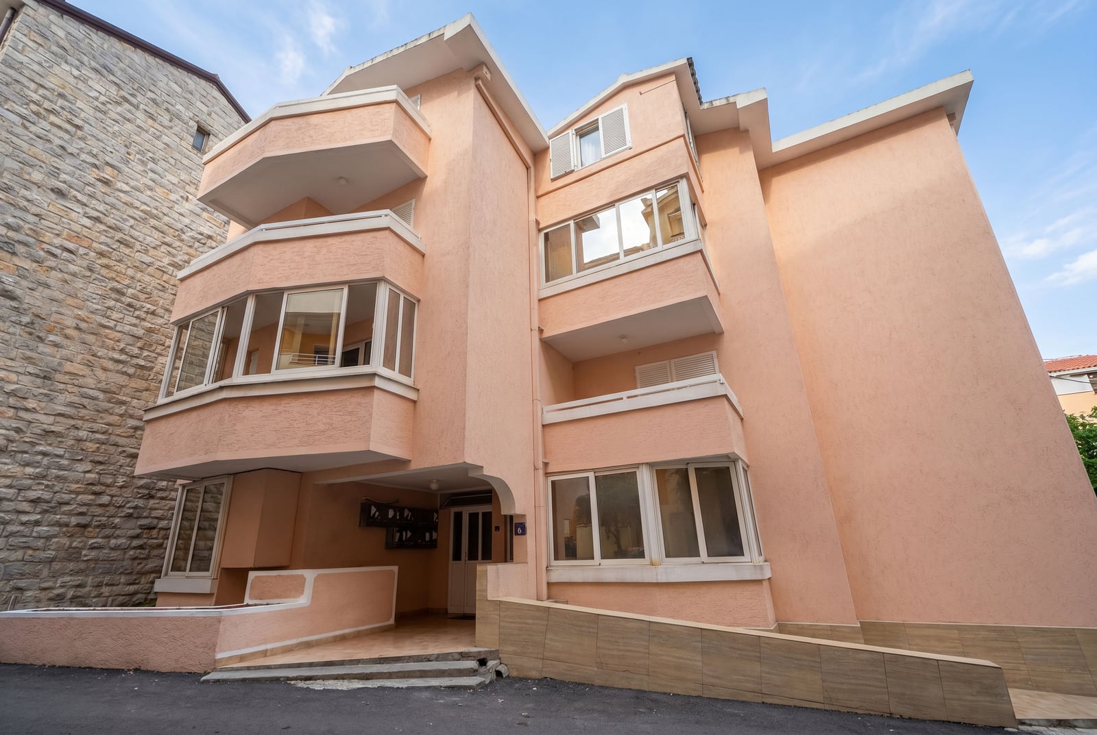 Facade of a modern peach-colored residential building with balconies and panoramic windows in the city of Budva, Montenegro.